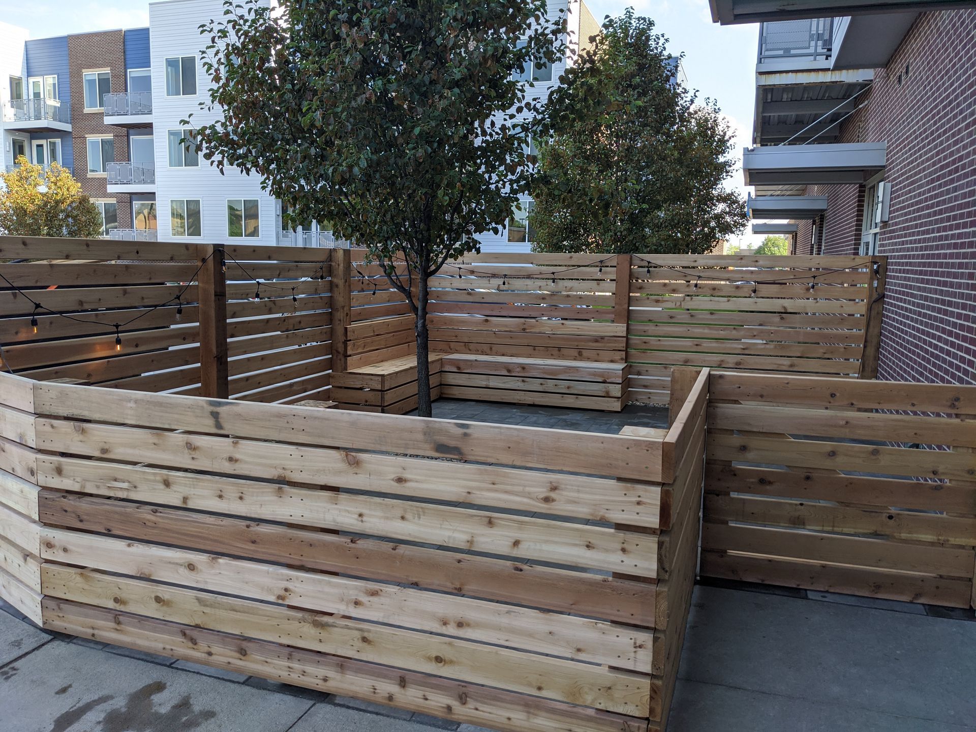 Wooden fence with a tree in the center, built on a concrete surface outside a building.