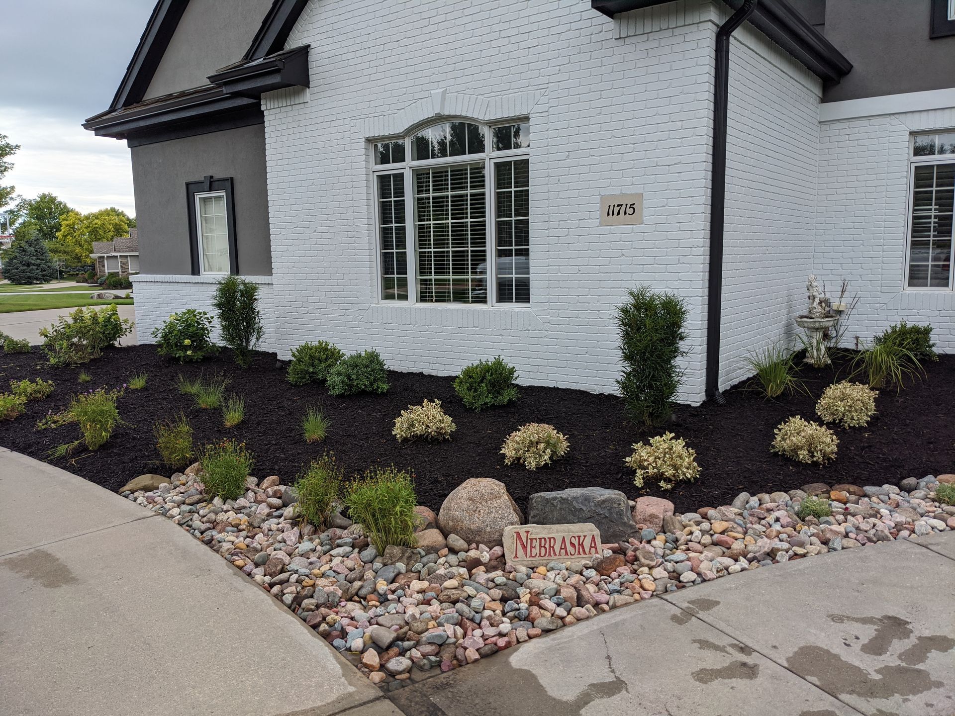 A brick home with a landscaped front yard featuring dark mulch, stones, and various shrubs.