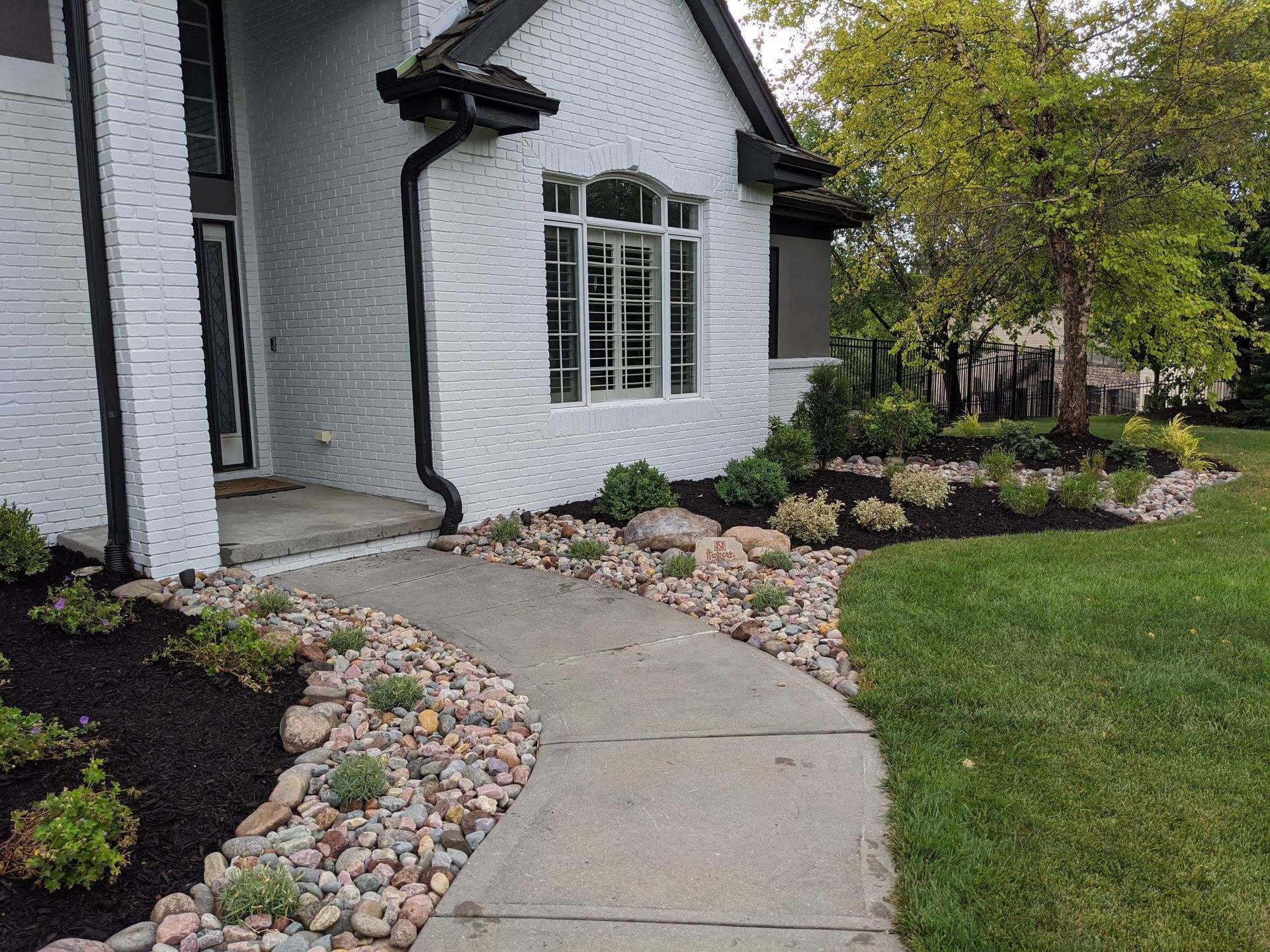 White brick house with landscaping, a stone path, and a green lawn.