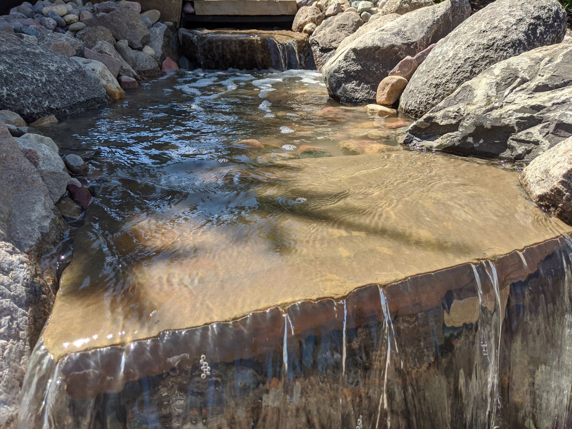 Water cascading over a rock ledge into a small pond surrounded by large rocks.