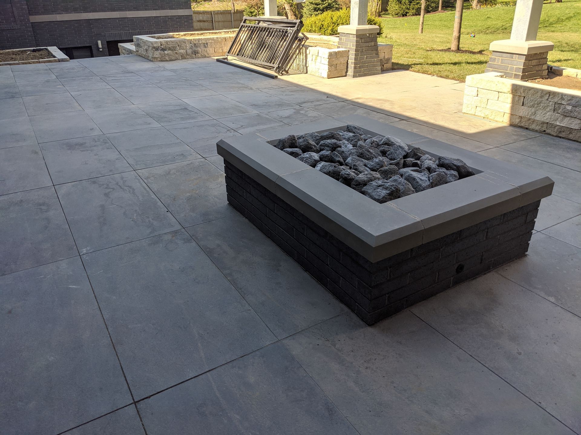 Gray stone fire pit on a gray stone patio with rock fill, surrounded by stone walls and columns.