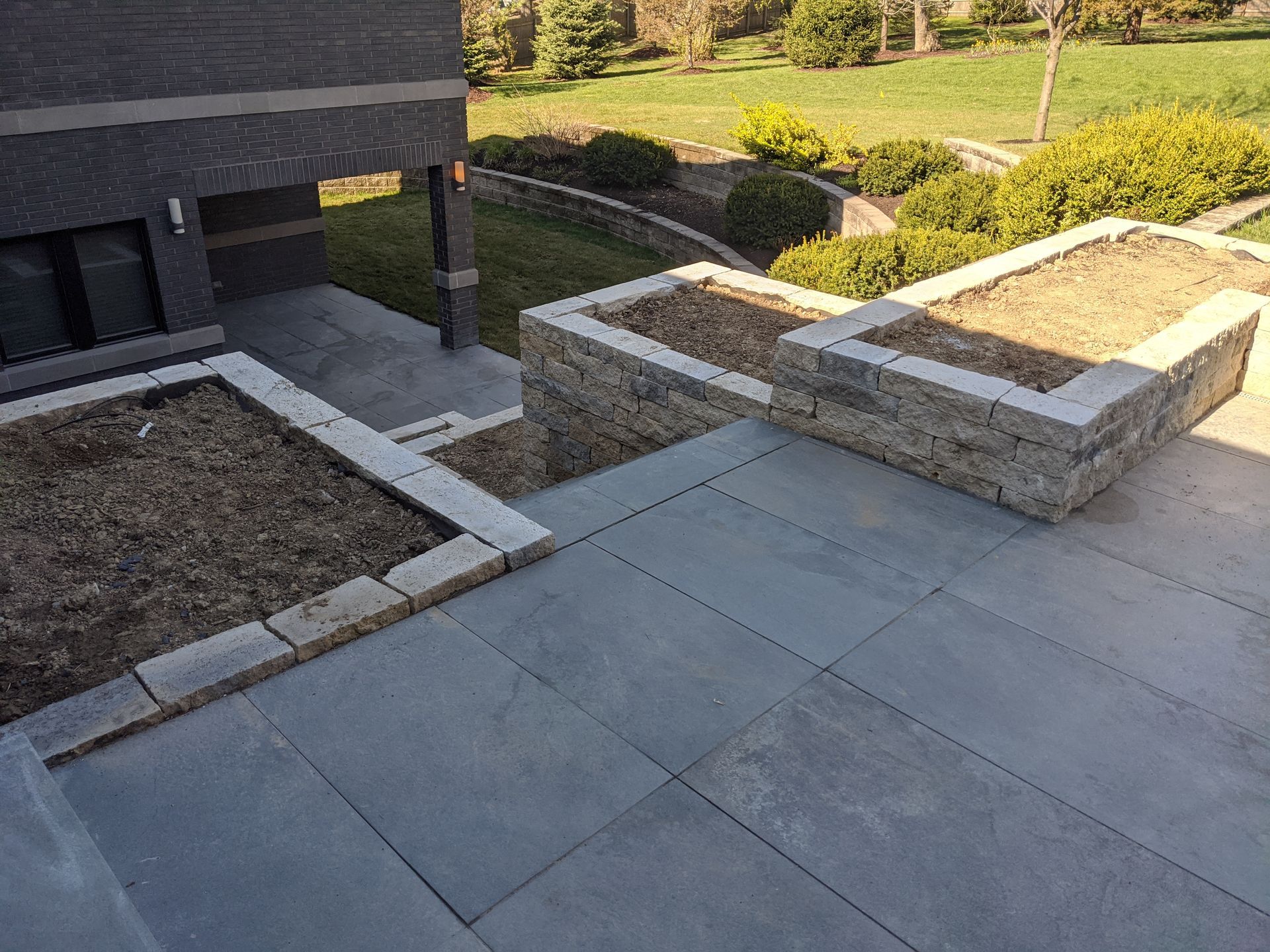 Stone patio with built-in planters, leading to a landscaped yard with green grass and shrubs.
