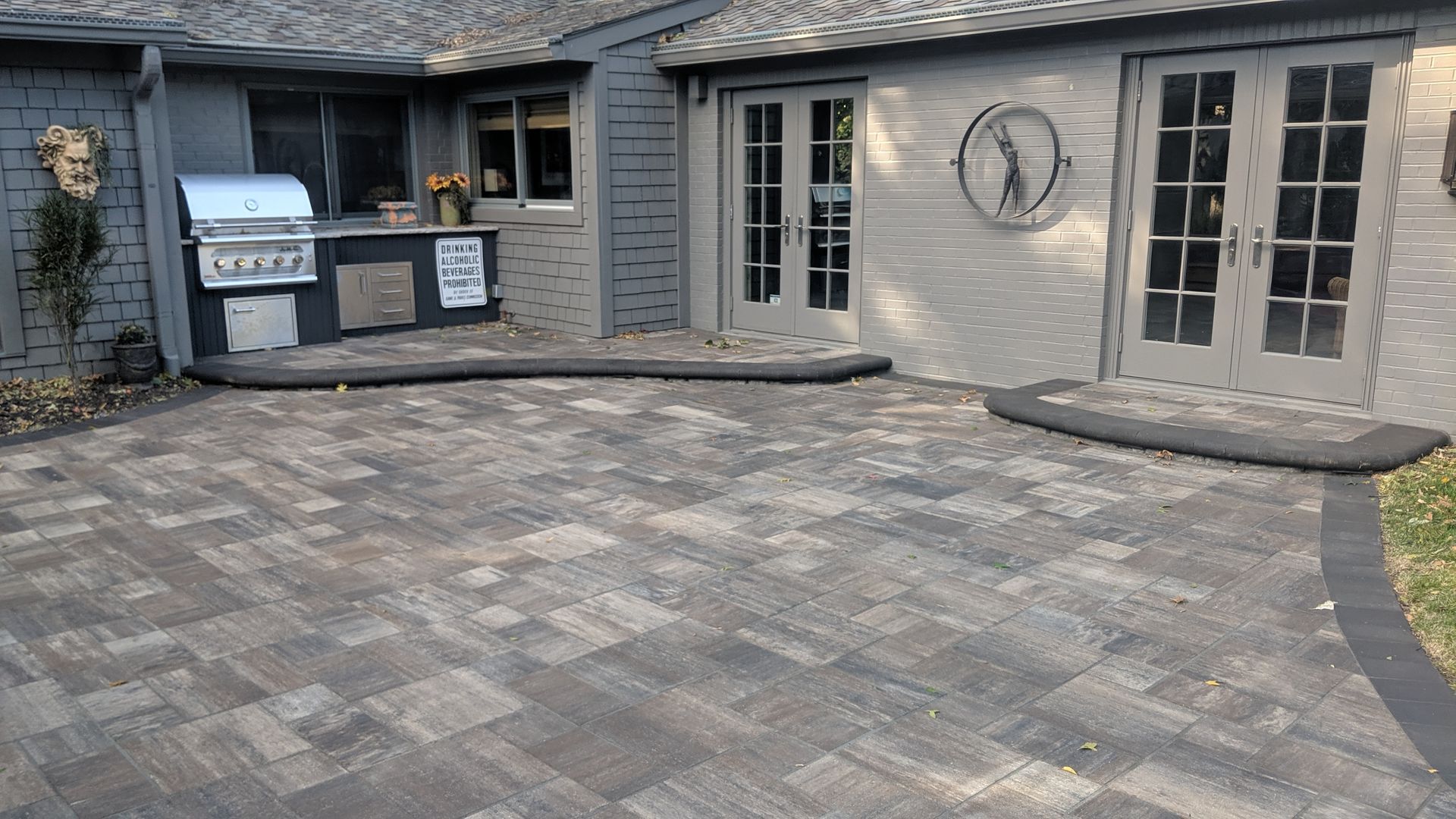 Paver patio with grilling station, double doors, and gray building exterior.