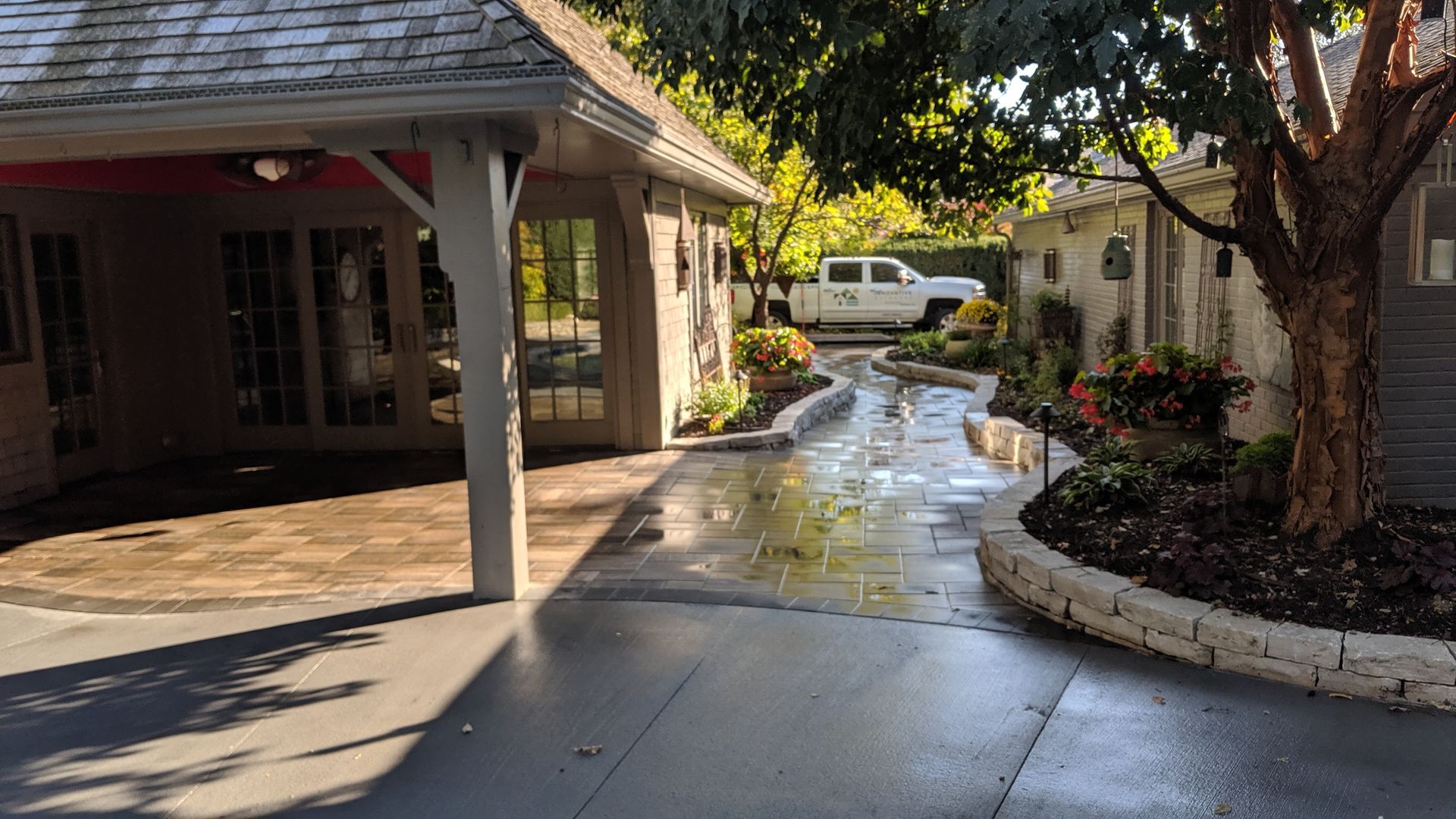 Driveway leading to a building with a carport and landscaping. A white truck is parked further down.