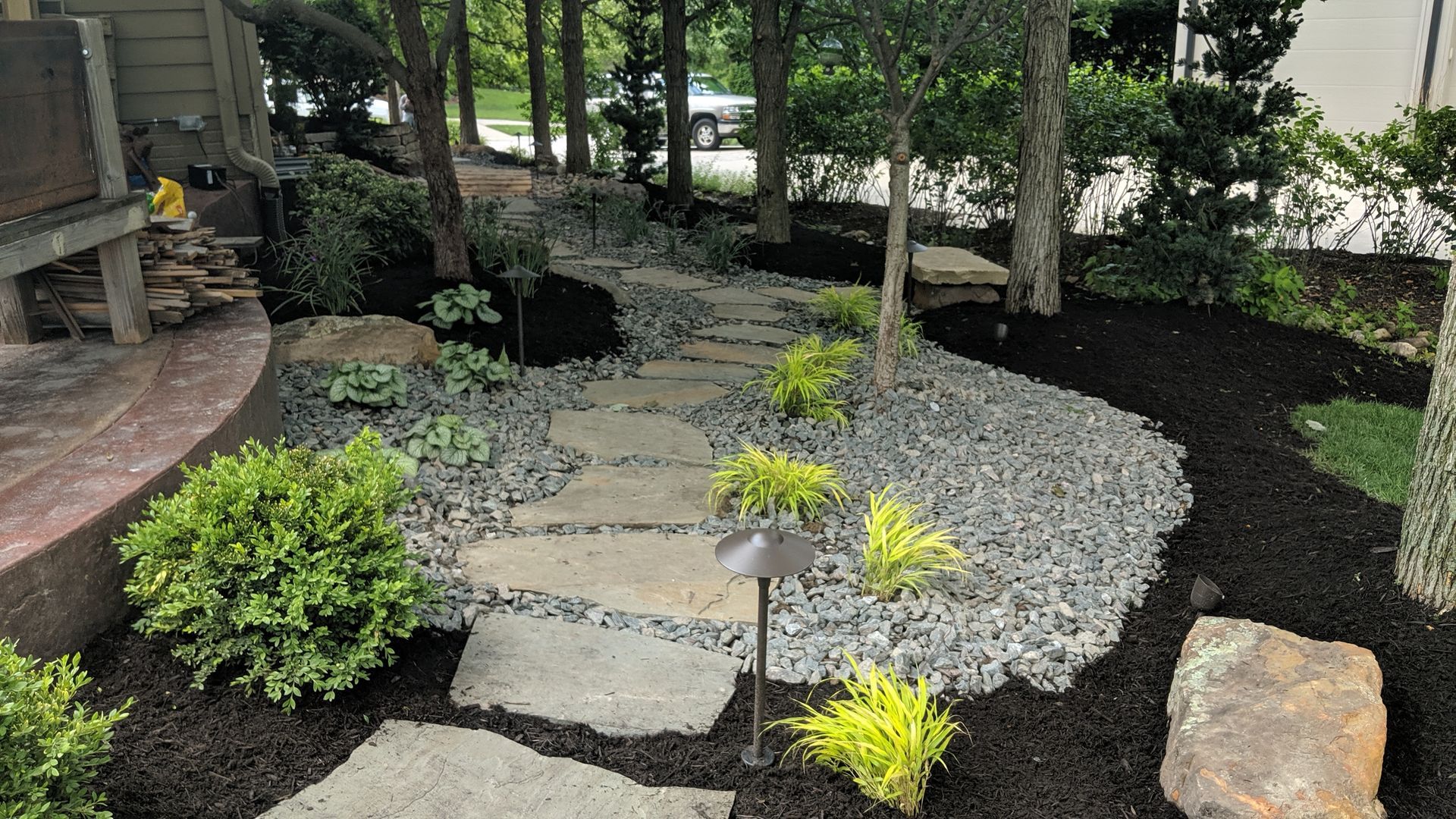Stone path through landscaped garden with mulch, gravel, trees, and shrubs.