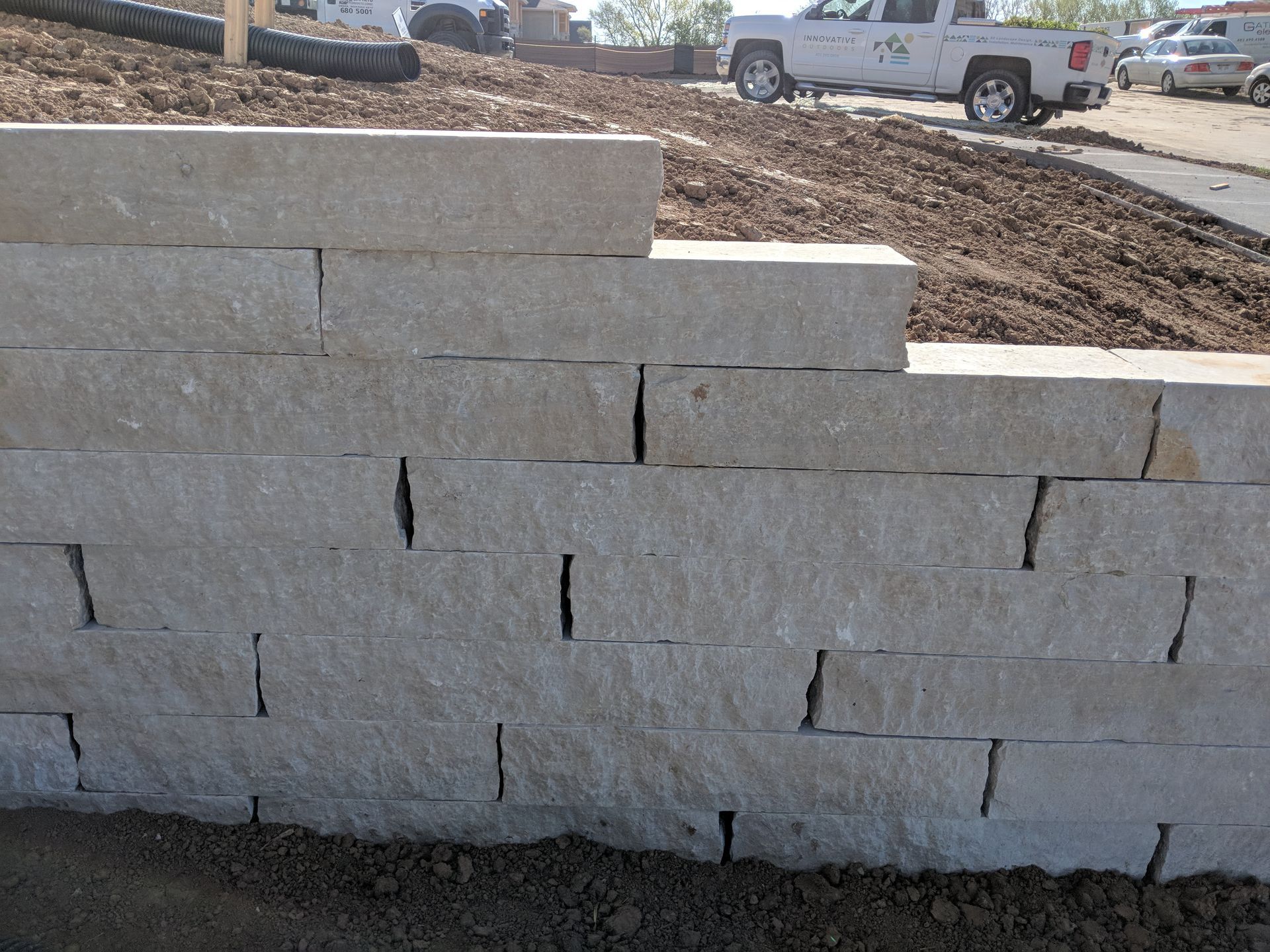 Stone retaining wall built on a slight slope, with a white pickup truck in the background.