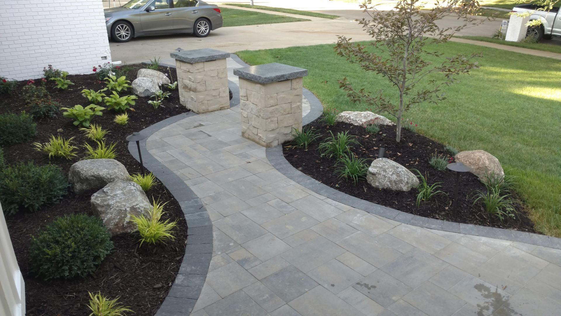 Stone path curves between garden beds and decorative stone pillars, leading to a front door.
