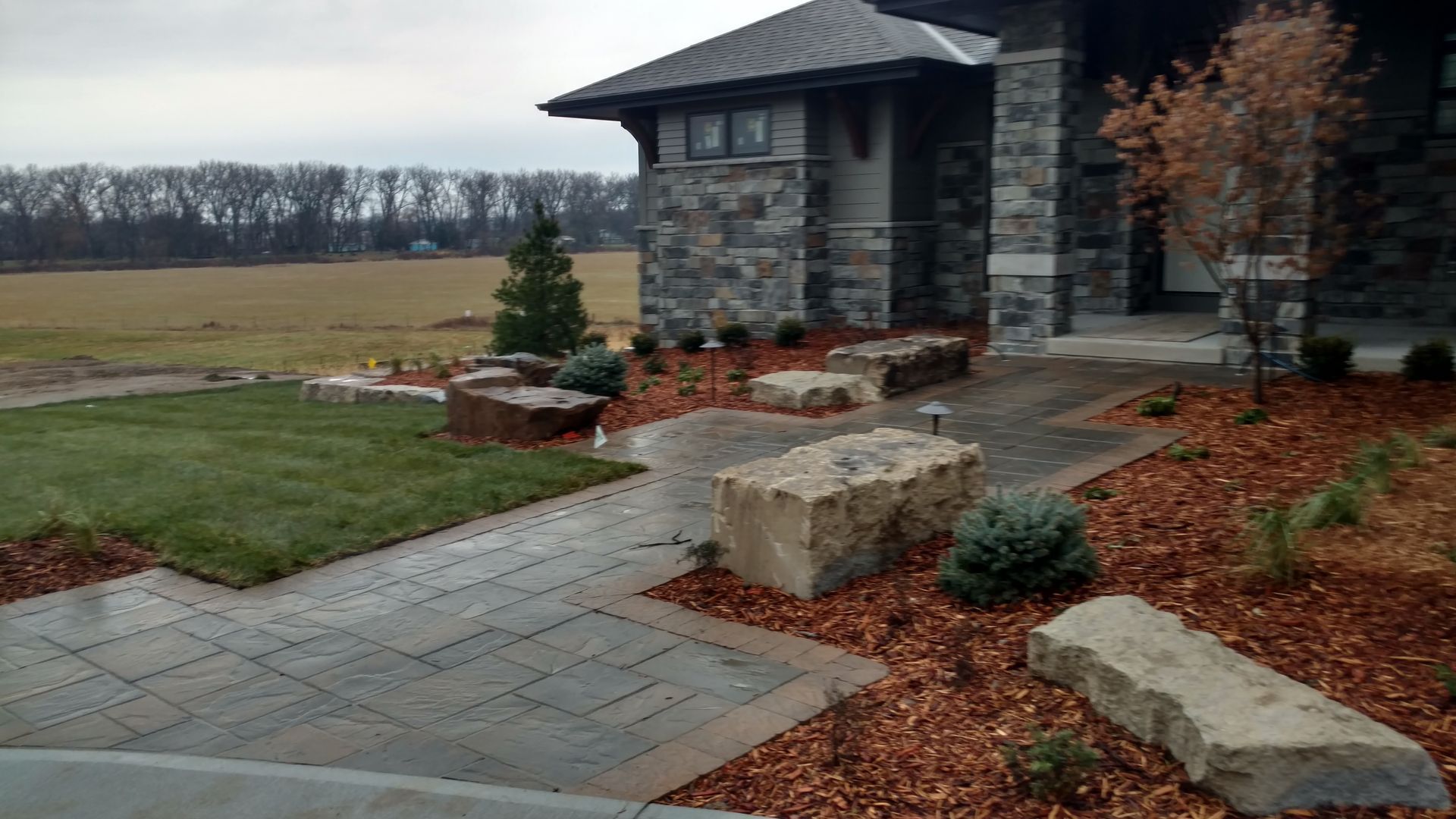 Stone path leads to a house with a stone facade, surrounded by landscaping and large rocks.
