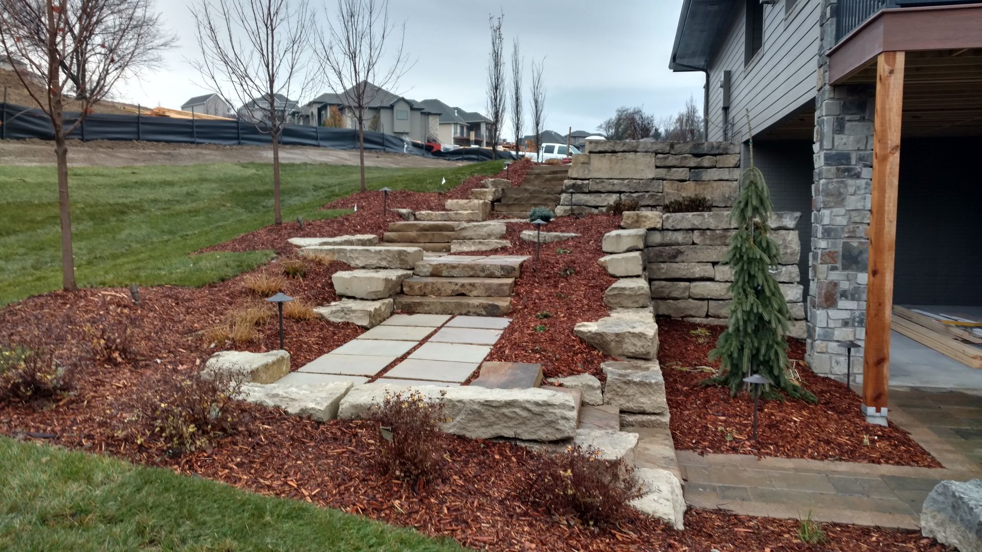 Stone steps and retaining walls on a hillside with mulch, landscaping, and a house.