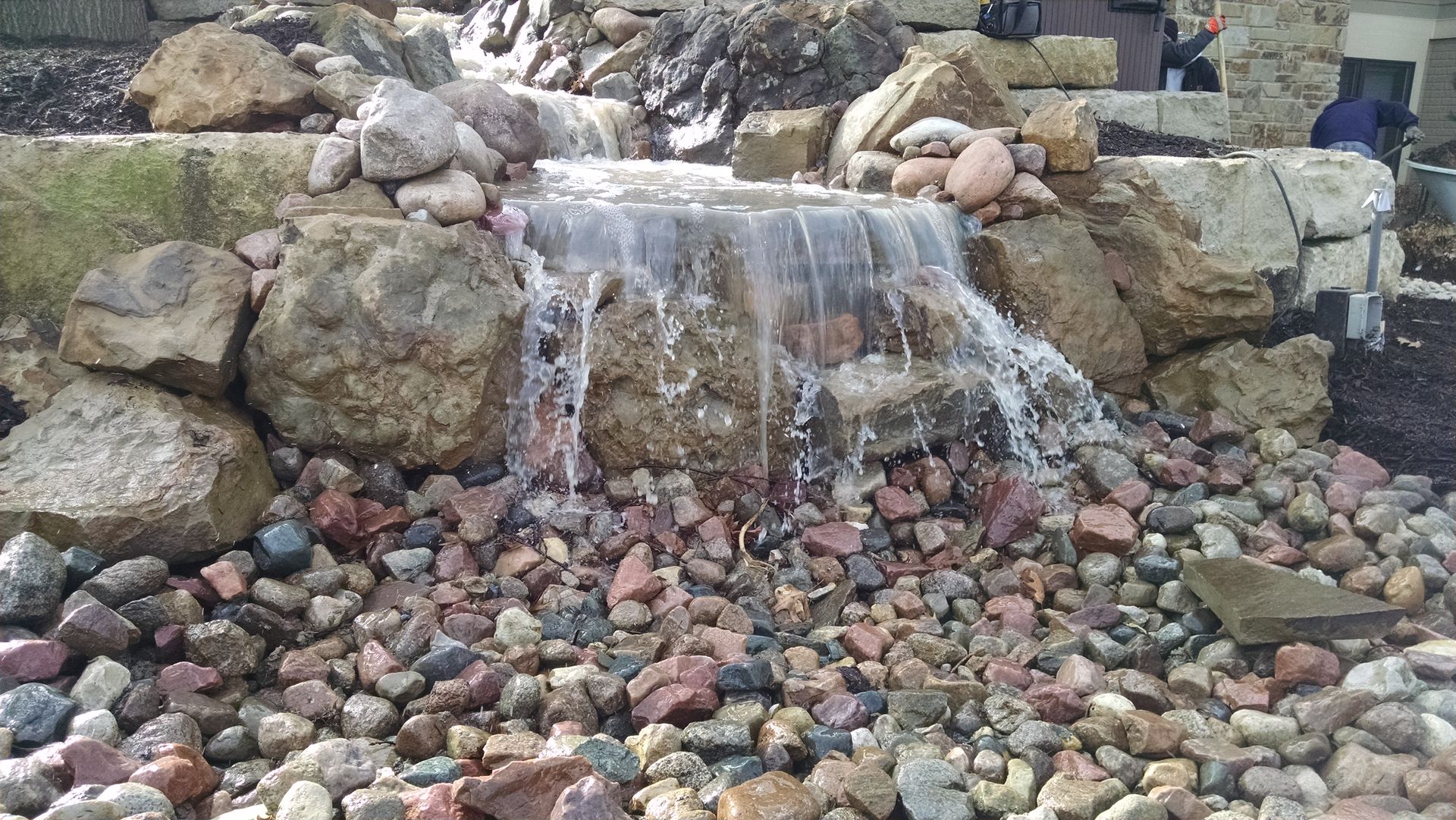 Waterfall cascading over rocks into a bed of colorful pebbles.