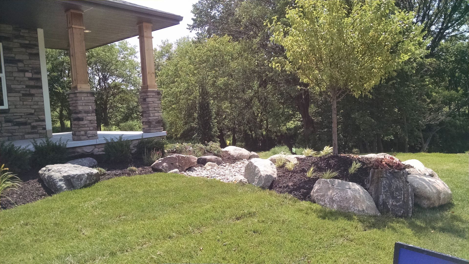 Front yard landscaping with boulders, a small tree, and a covered porch.