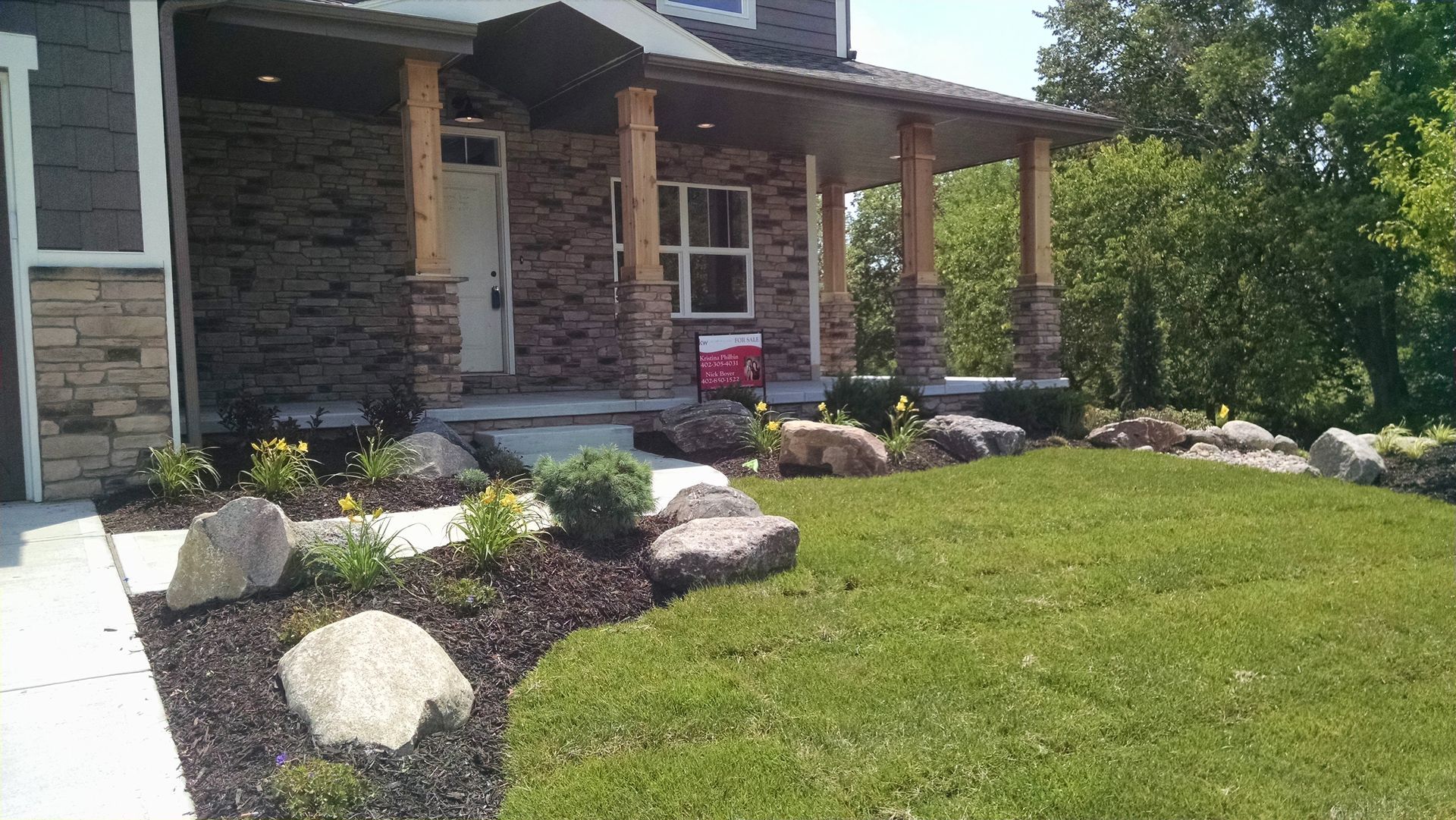 A house with a porch, surrounded by a landscaped yard with rocks, mulch, and green grass.