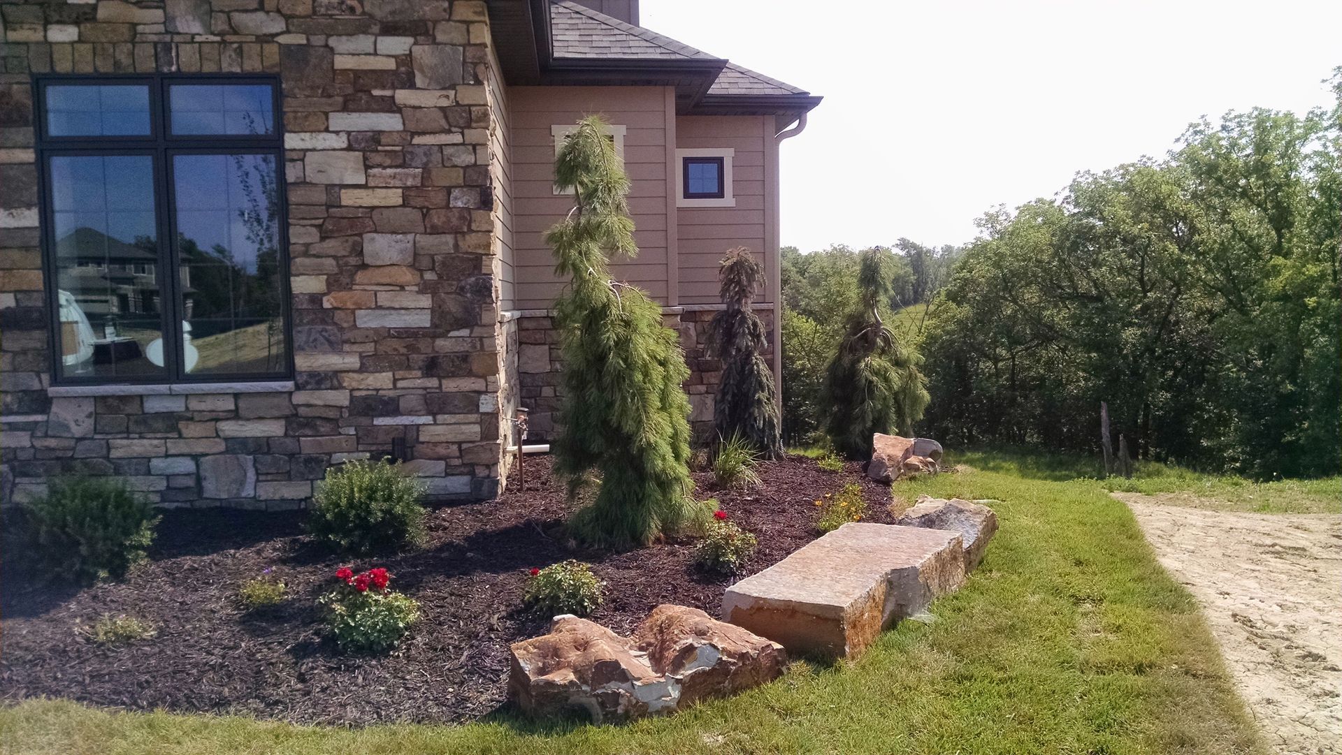 Exterior view of a house with stone siding, landscaping, and a grassy area.