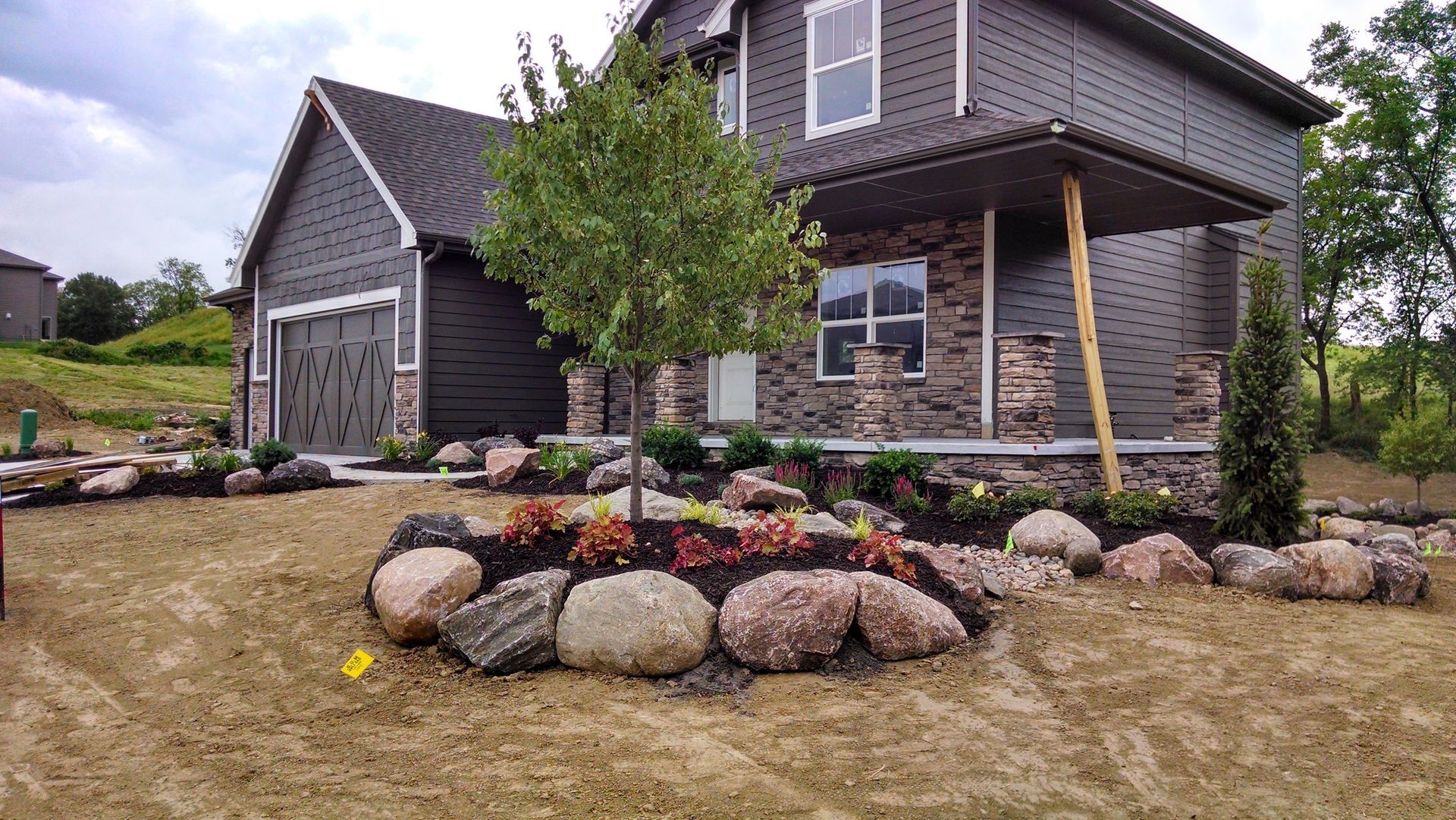 Modern home with dark gray siding, a stone facade, and a landscaped yard with large rocks.