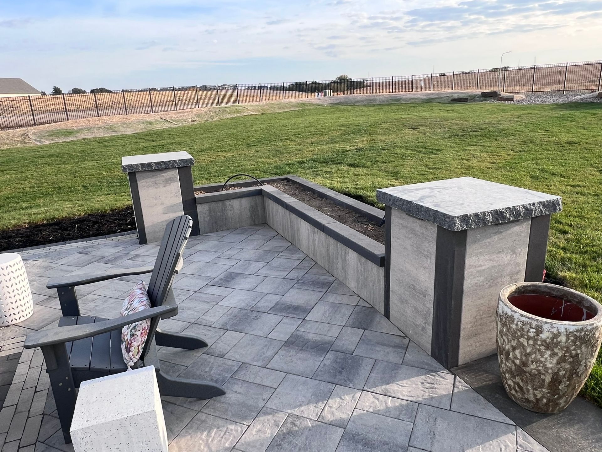 Patio with gray pavers, built-in planters, two pillars, Adirondack chair, and a large decorative pot.