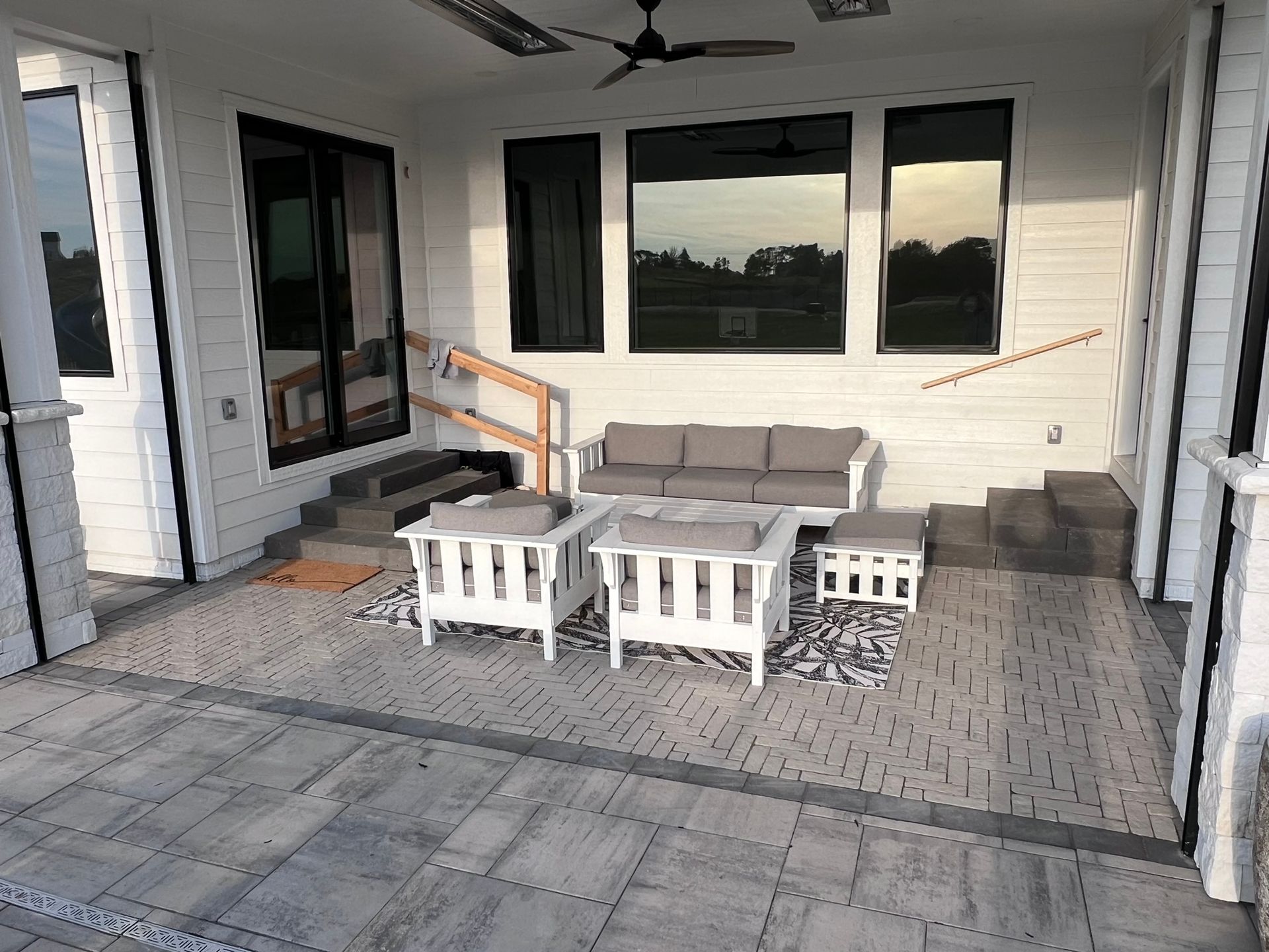 Outdoor patio with white furniture, gray pavers, and large windows.