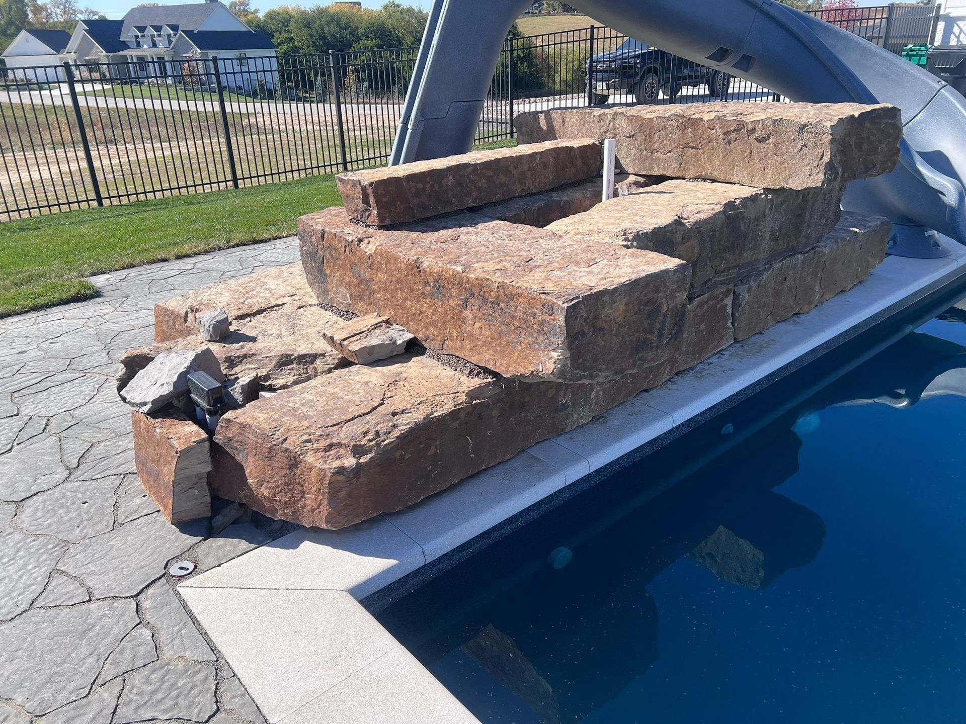 Stone steps and retaining wall next to a pool with a slide, sunny day.