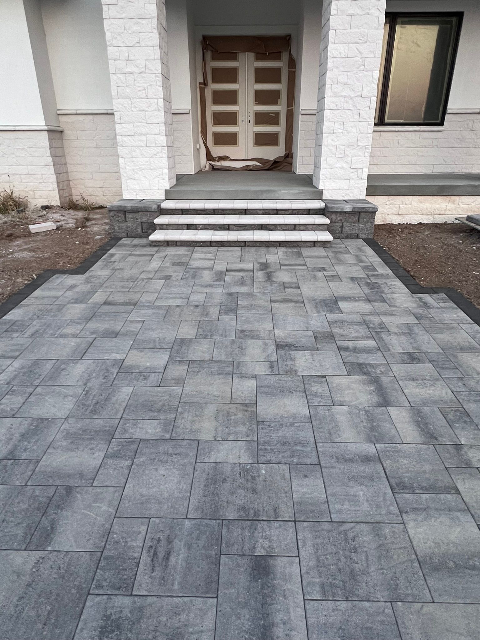 Gray stone paved walkway leading to a house entrance with steps.