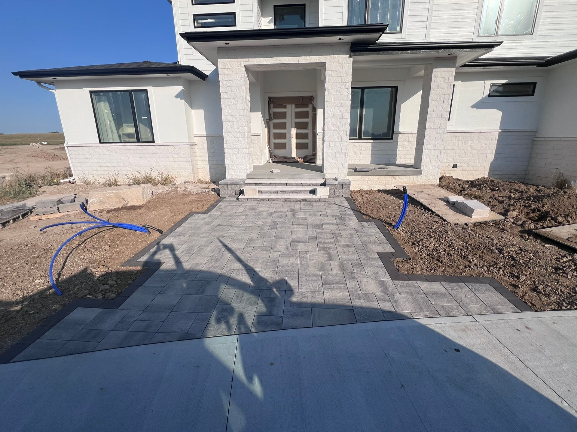 Exterior of a house with a gray paved walkway leading to the front door; construction debris present.