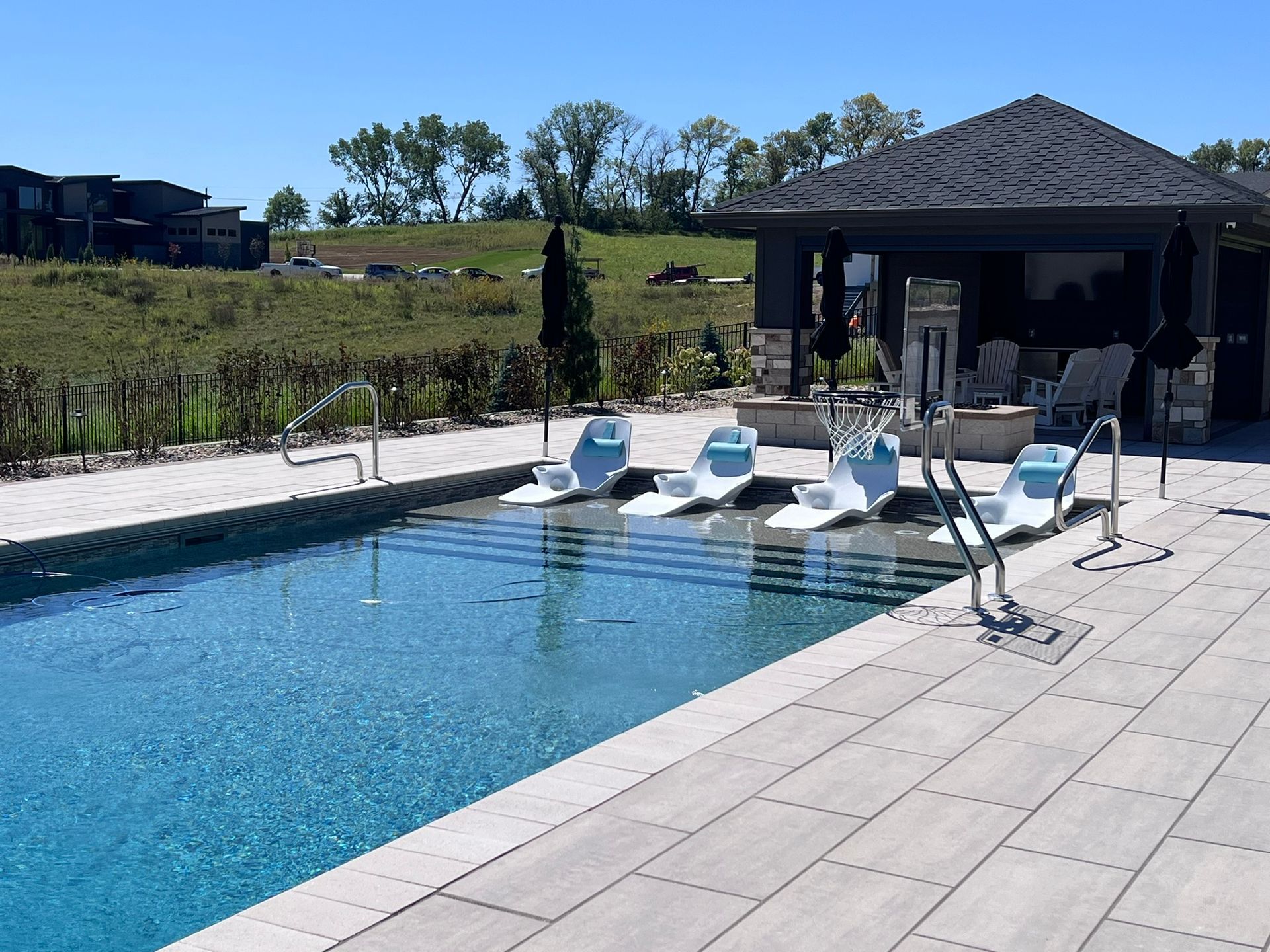 Pool with swim-up loungers, patio, and gazebo, against a sunny, green landscape.