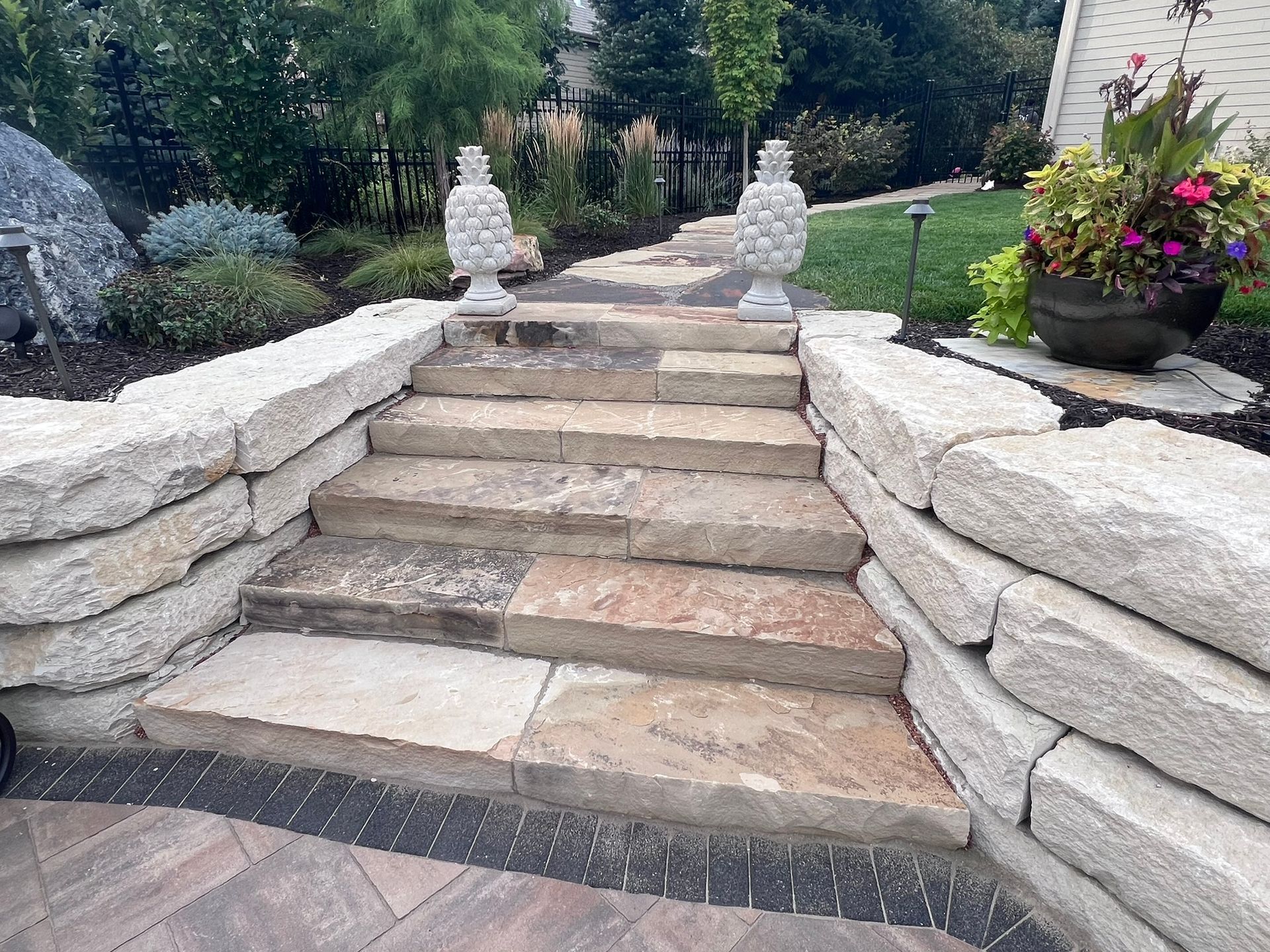 Stone steps with retaining walls lead to a pathway with two decorative urns.