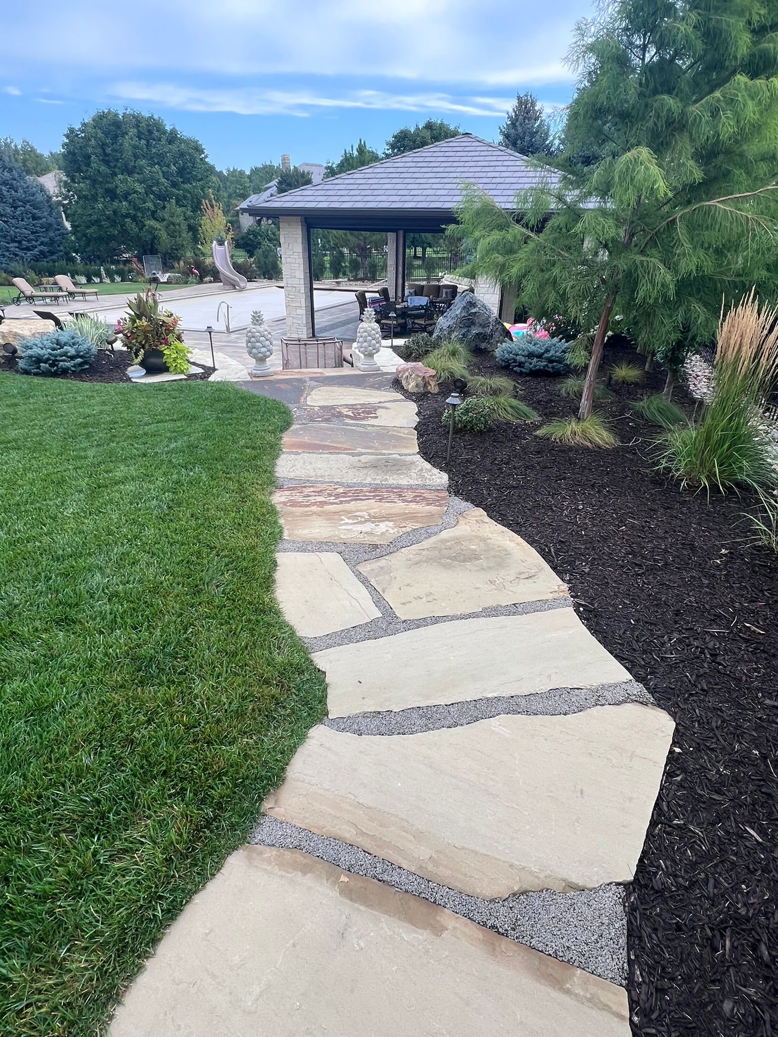 Stone path through green lawn and mulch garden leads to a gazebo.