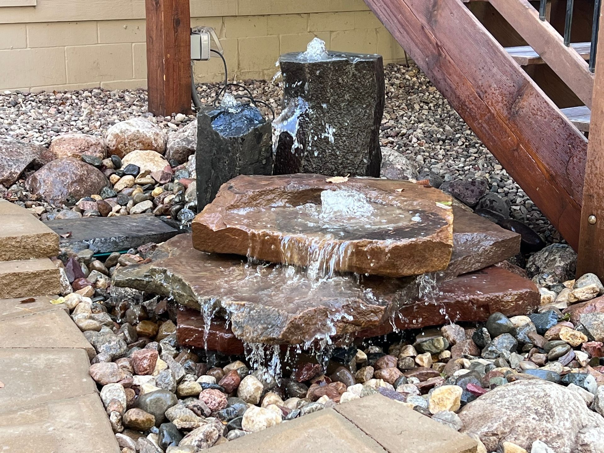 Water fountain made of stacked stones, water flowing over rocks in a garden setting.
