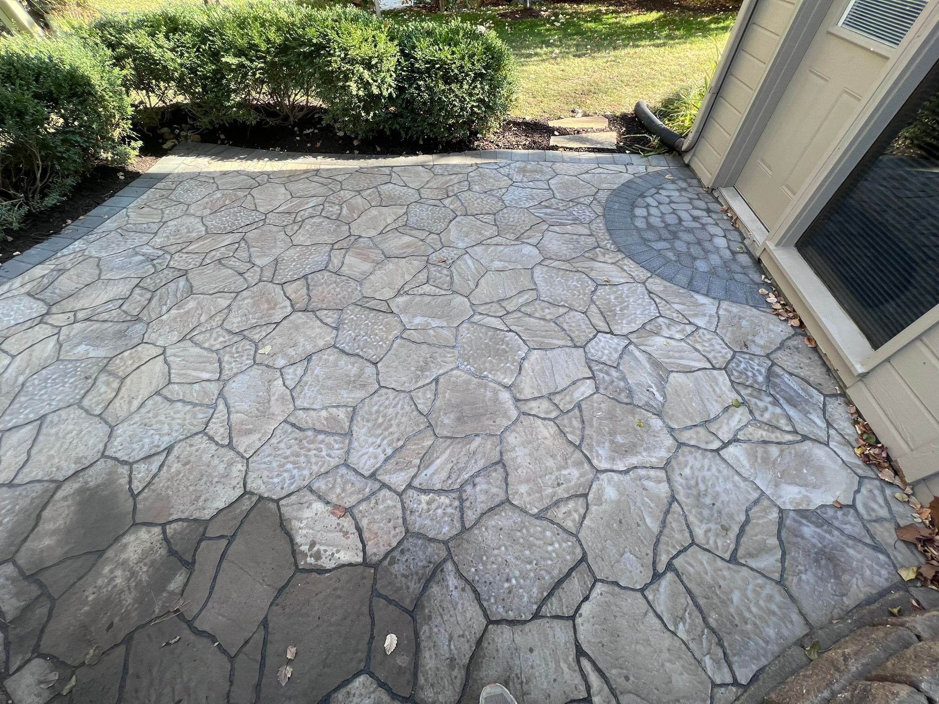 Patio paved with irregular stones in various shades of gray, next to a building and greenery.