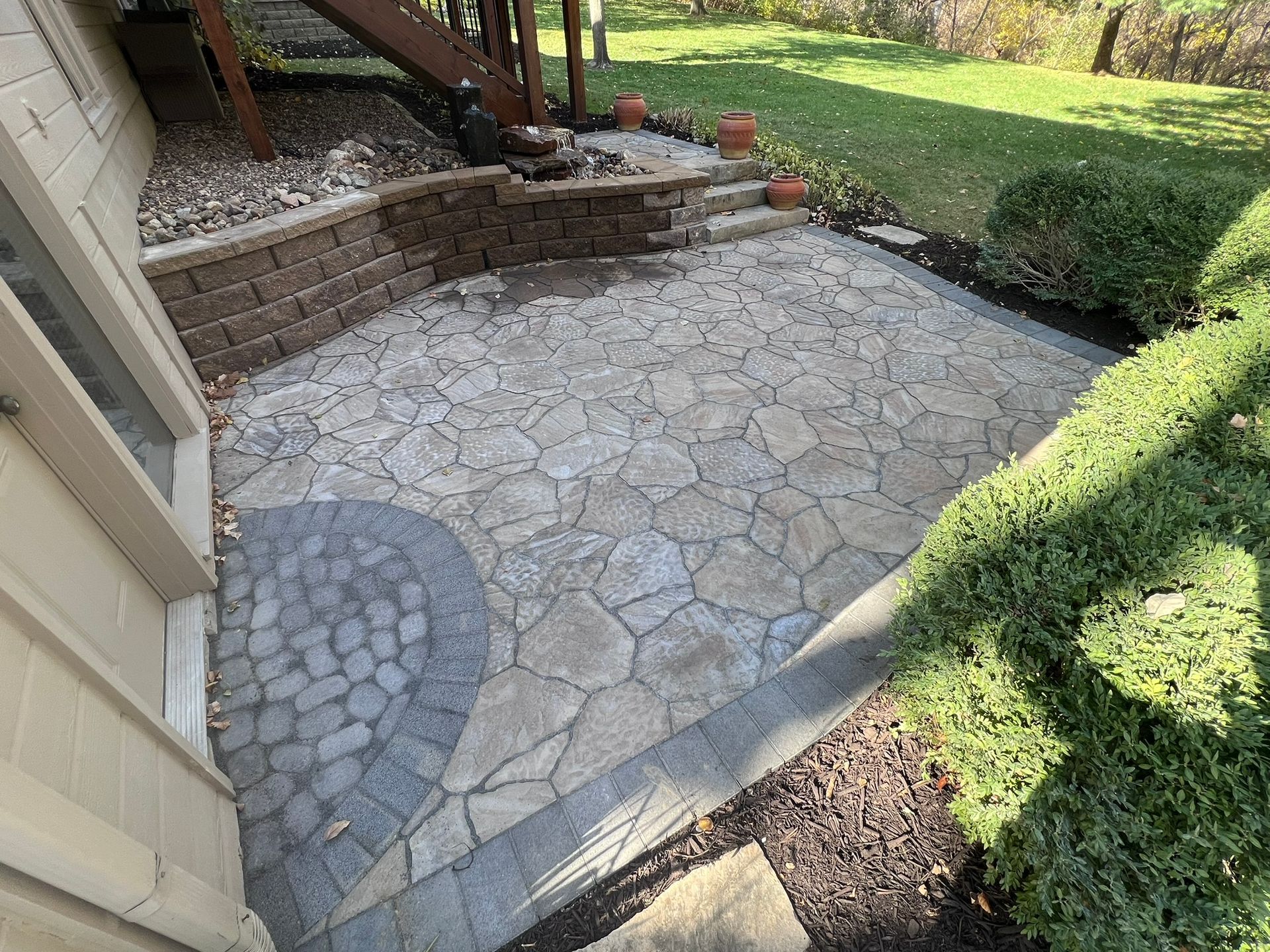 Stone patio next to a house with a small retaining wall and steps.