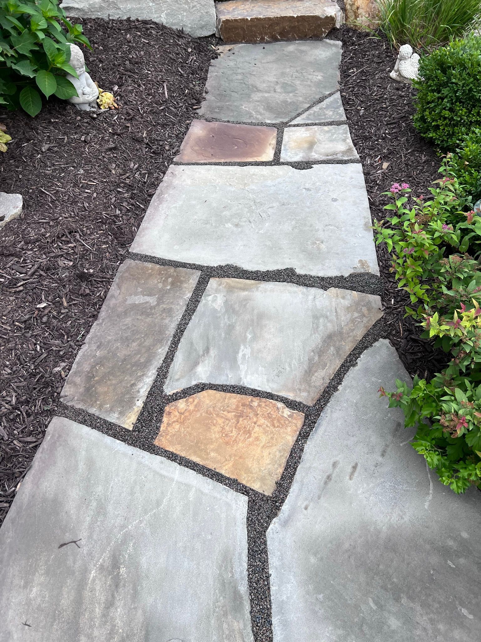 Flagstone walkway with dark mulch and plants on either side.