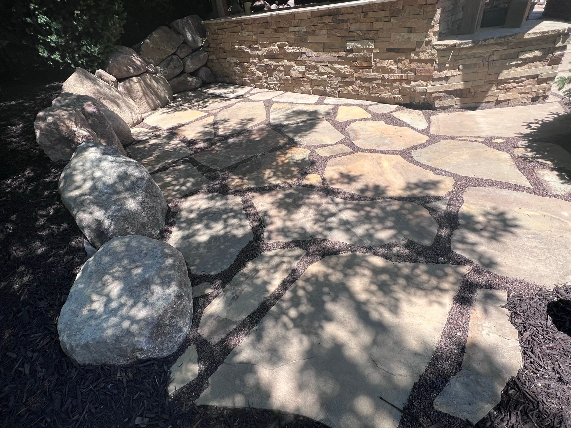 Stone patio with large rocks, stone retaining wall, and seating area.