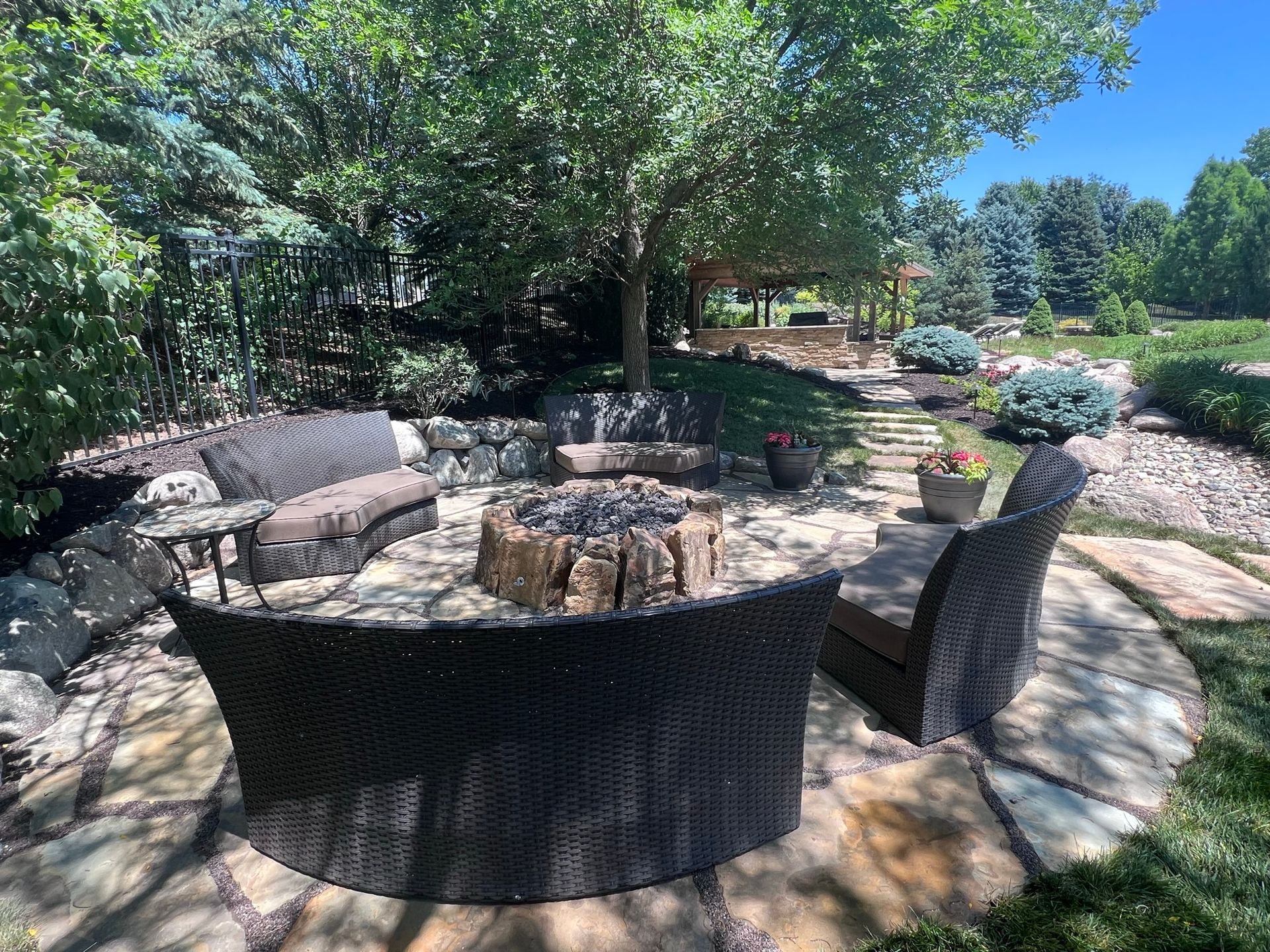 Cozy outdoor fire pit area with wicker furniture, surrounded by stone and greenery.