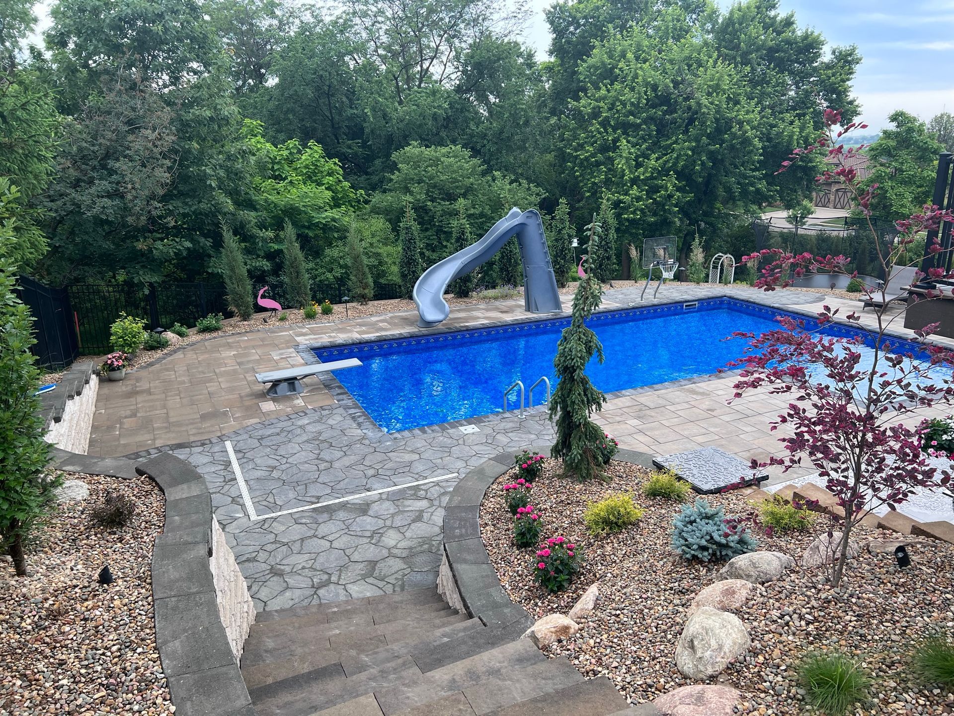 Backyard pool with a slide, diving board, and landscaping.