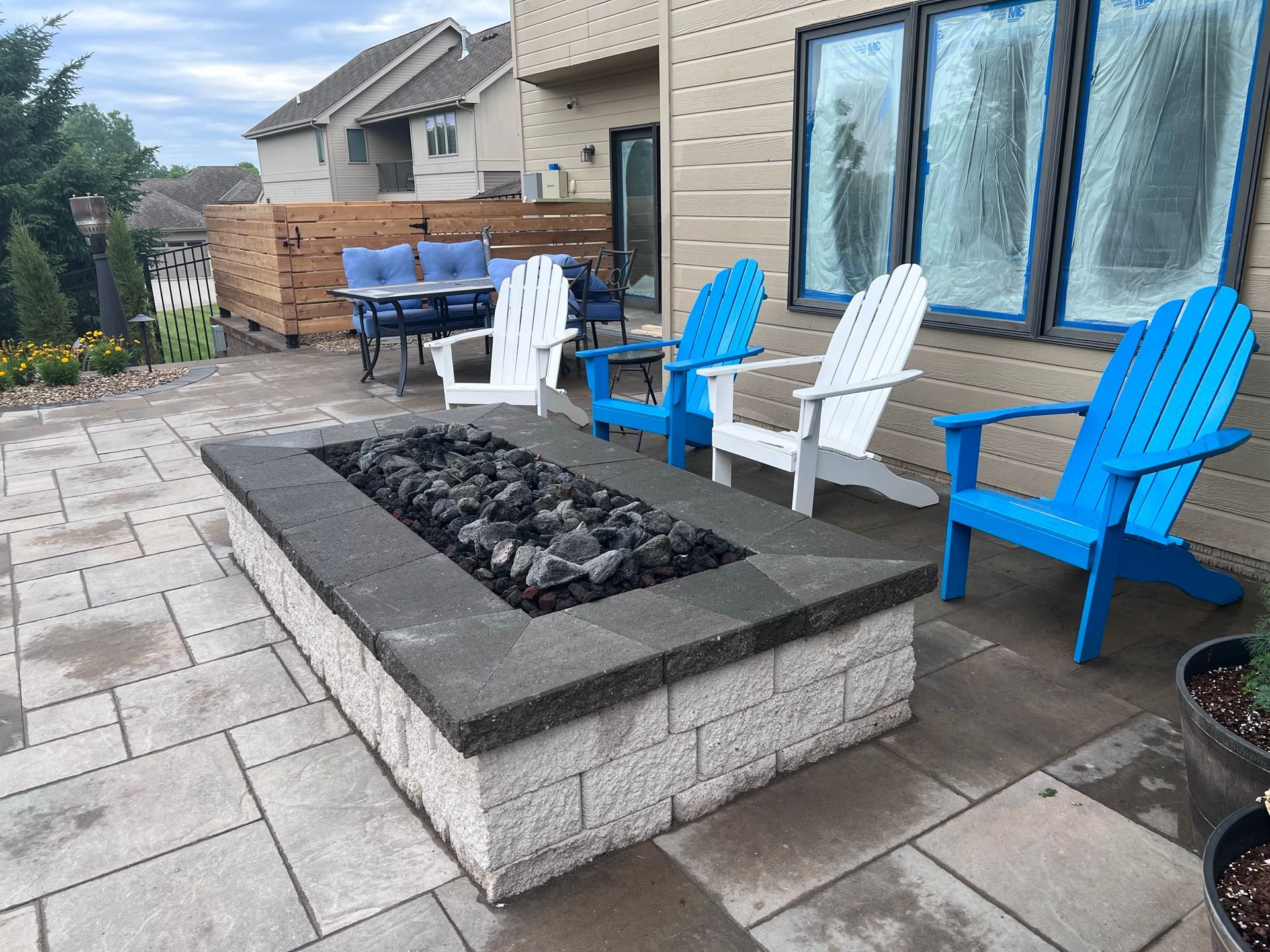 Patio with fire pit, Adirondack chairs (white and blue), and outdoor seating near a building.