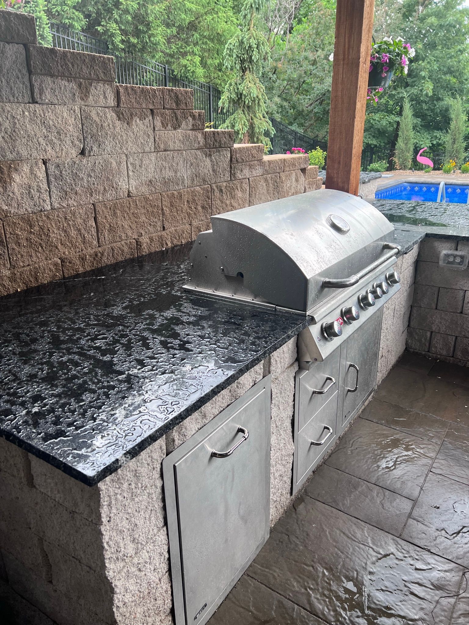 Outdoor kitchen with stainless steel grill on a black countertop, built into a stone structure.