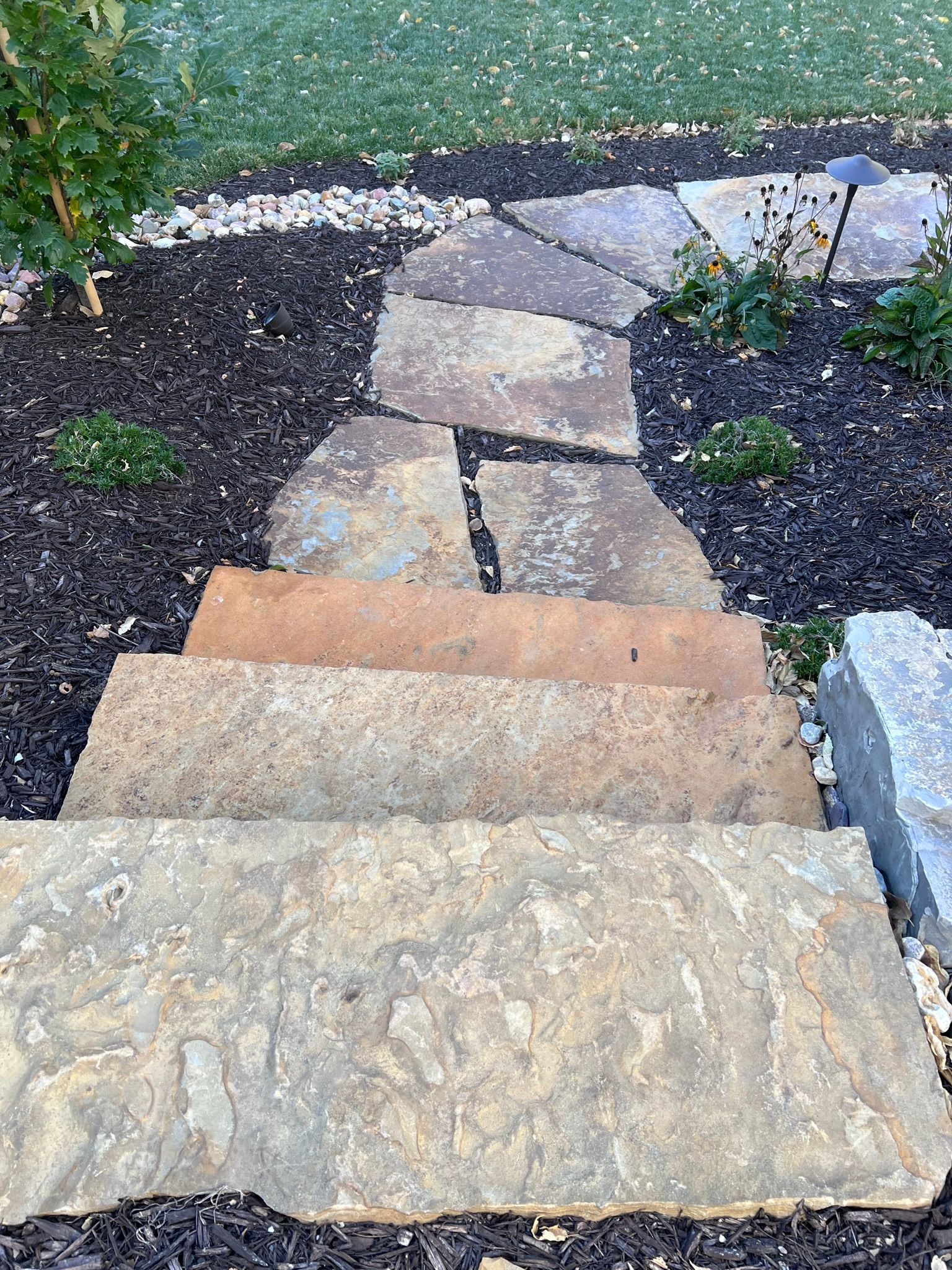Stone steps and walkway leading through dark mulch and a grassy area.