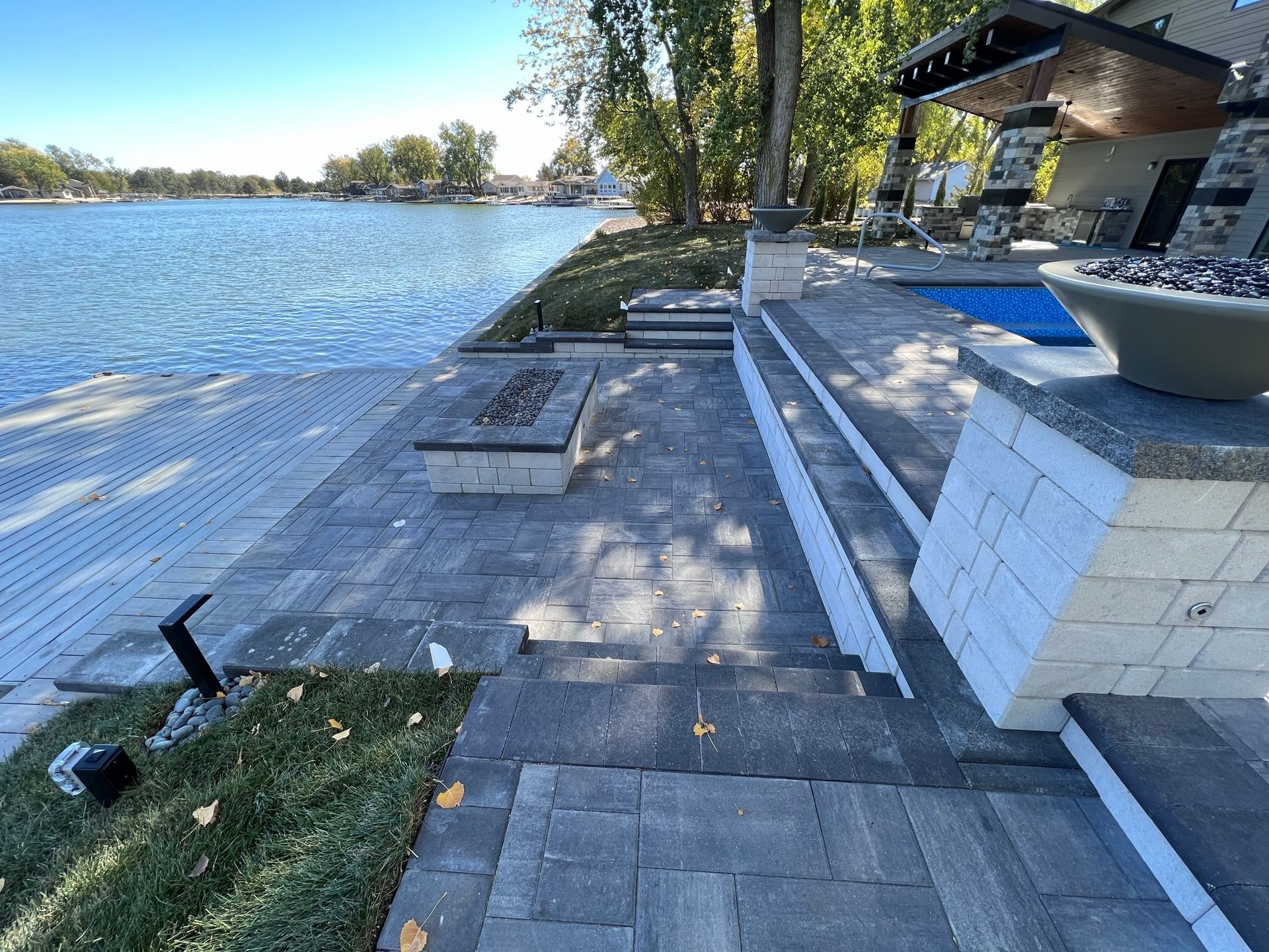 Patio with lake view, fire pit, stone steps, and building with a pool.