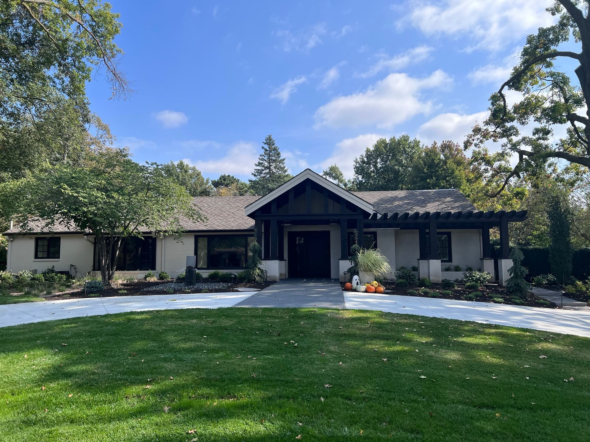 Exterior view of a ranch-style house with a dark wooden entry and a green lawn. Blue sky.