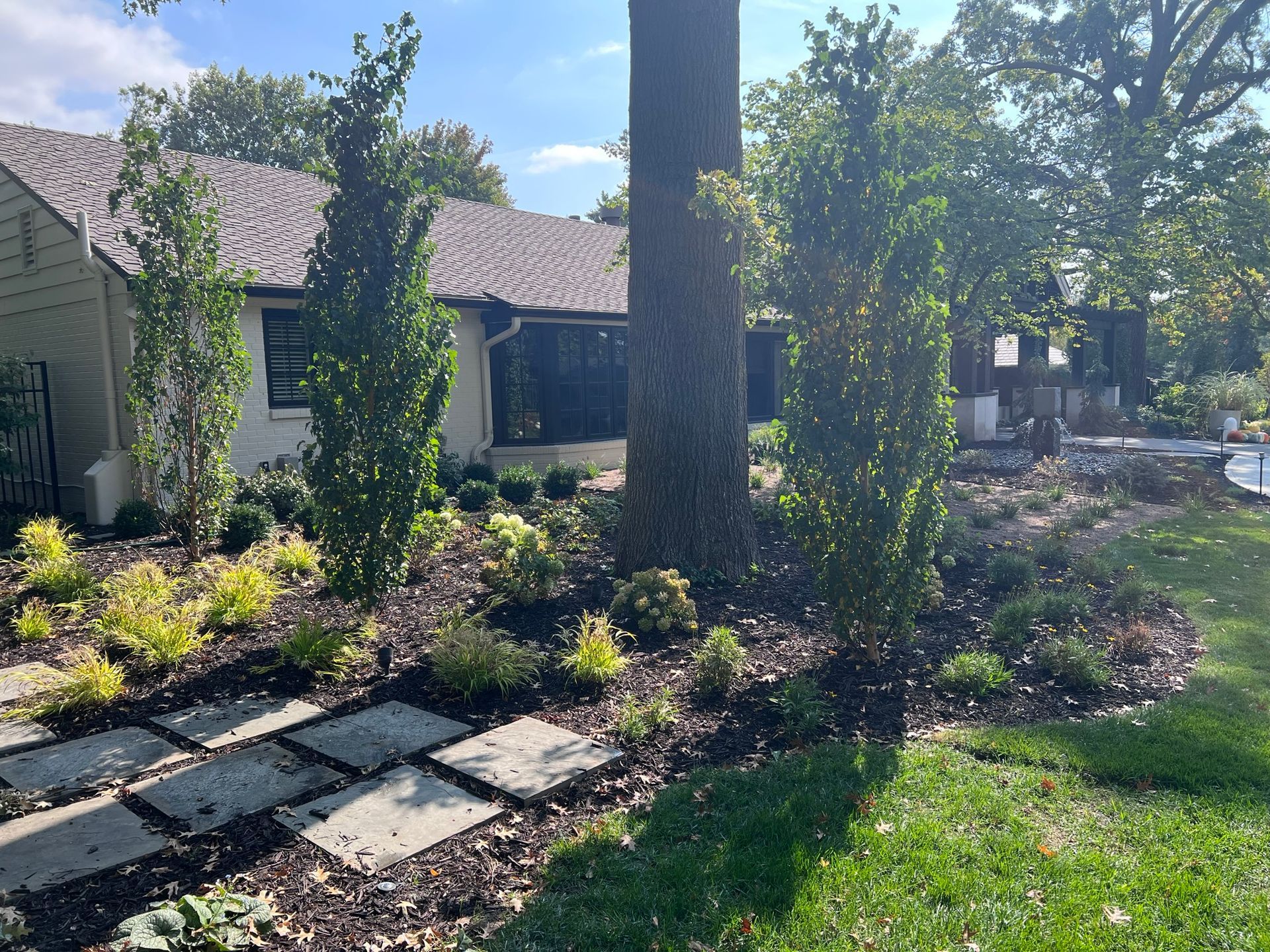 Stone path leads to a house with landscaping, trees, and shrubs on a sunny day.