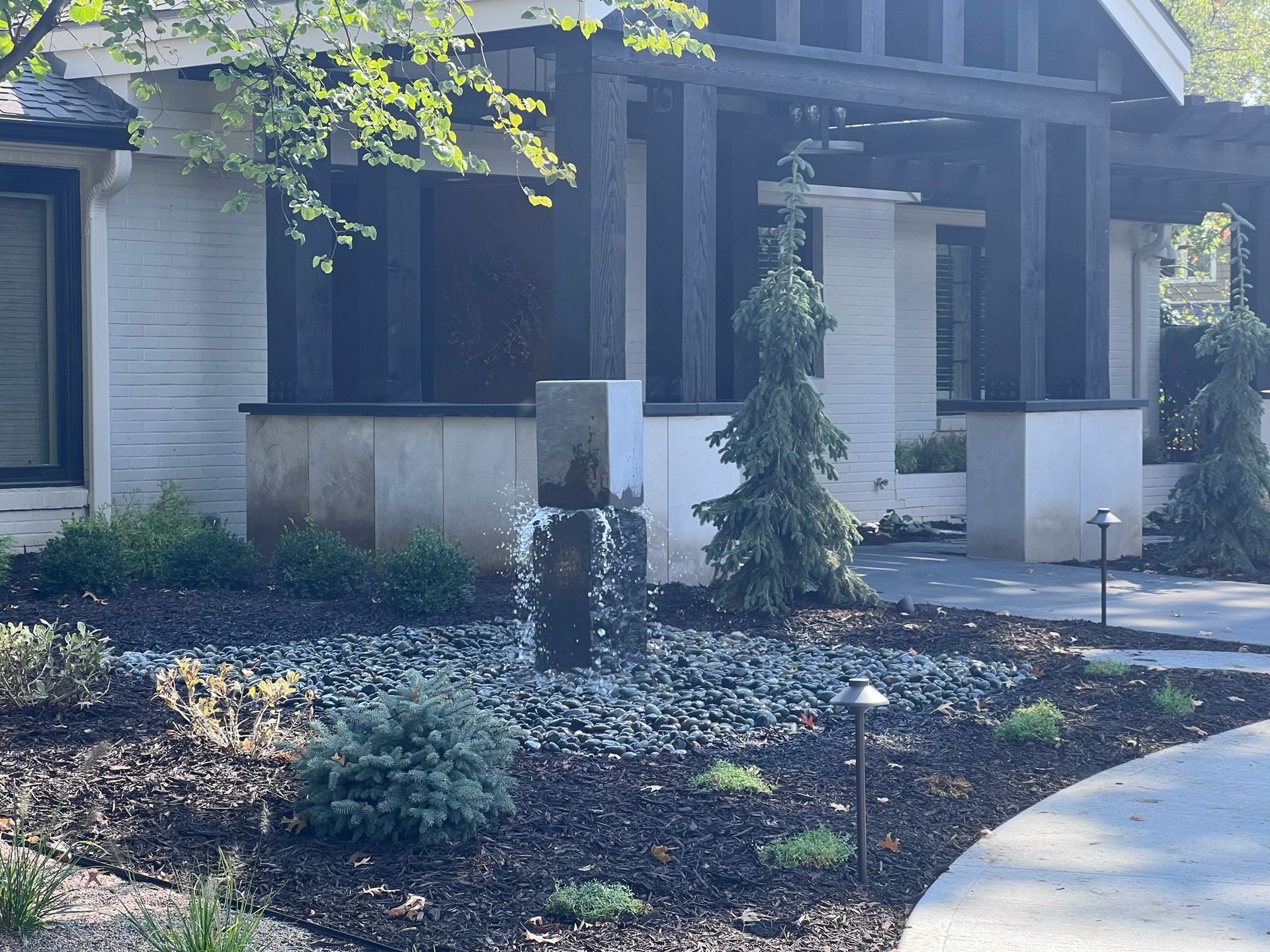 A modern home's exterior with a water feature, evergreen trees, and dark mulch landscaping.