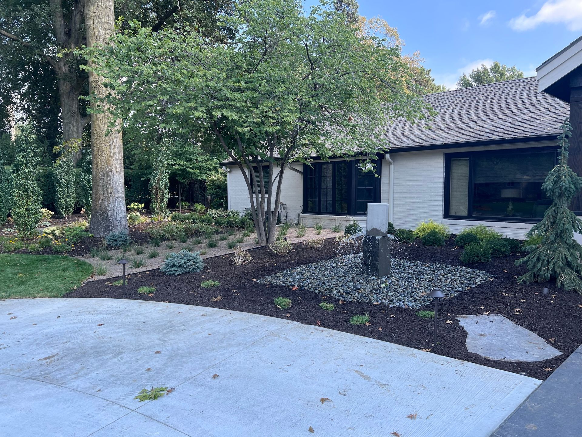 Landscaped front yard with a fountain, trees, and a white house with dark windows.