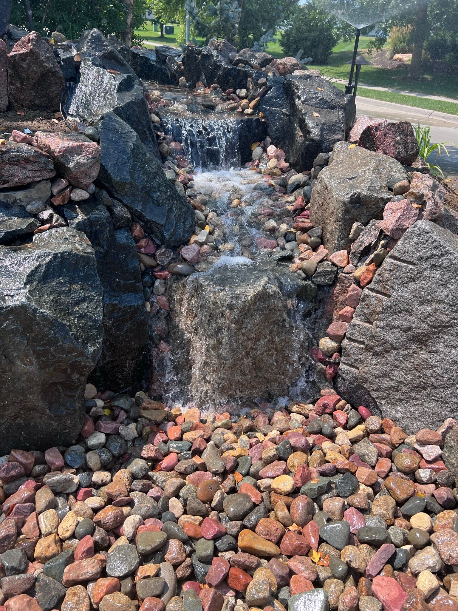 Water cascading down a rock waterfall feature with multi-colored stones.