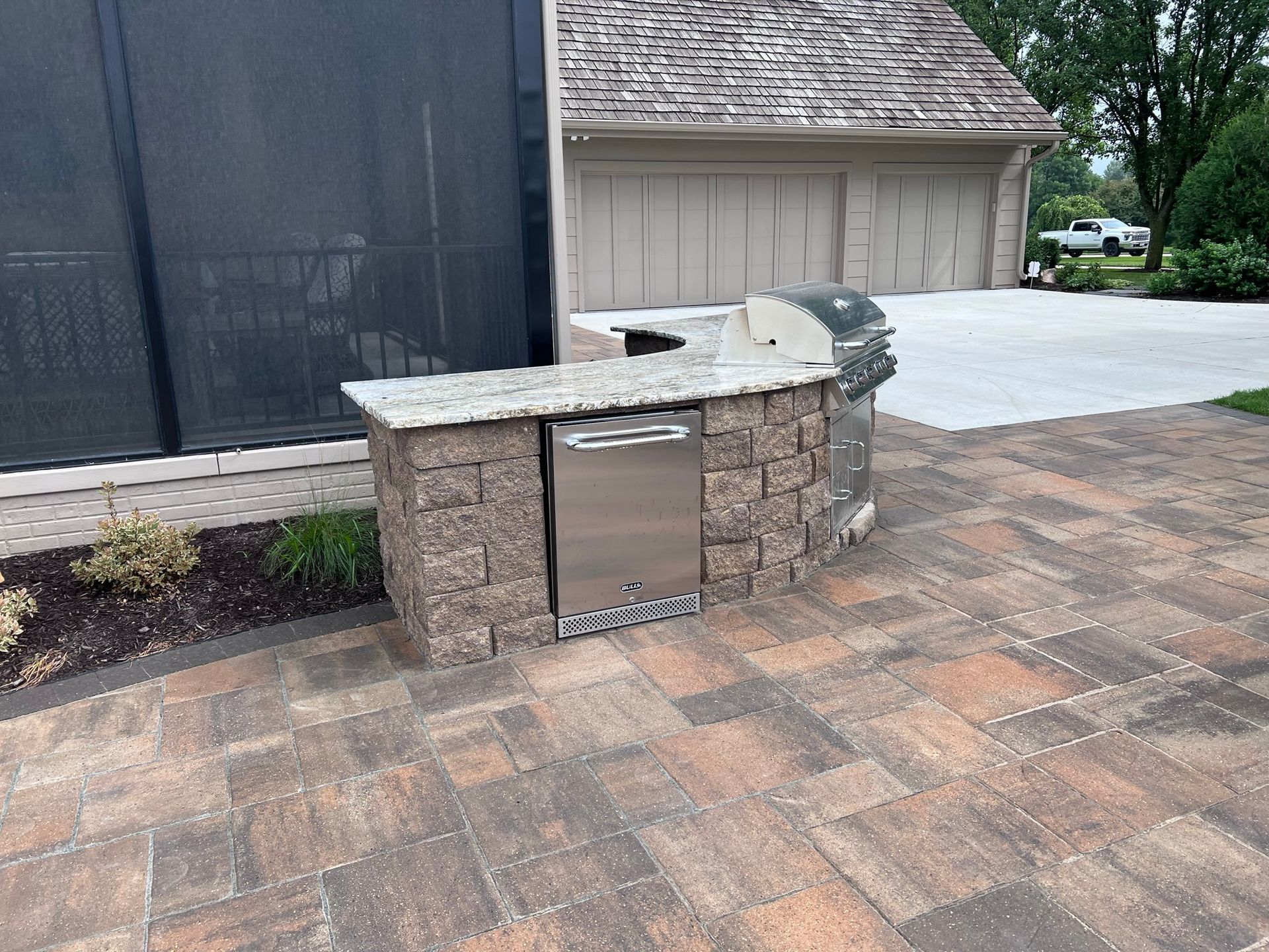 Outdoor kitchen with stone brick, grill, refrigerator, and granite countertop on a brick patio.