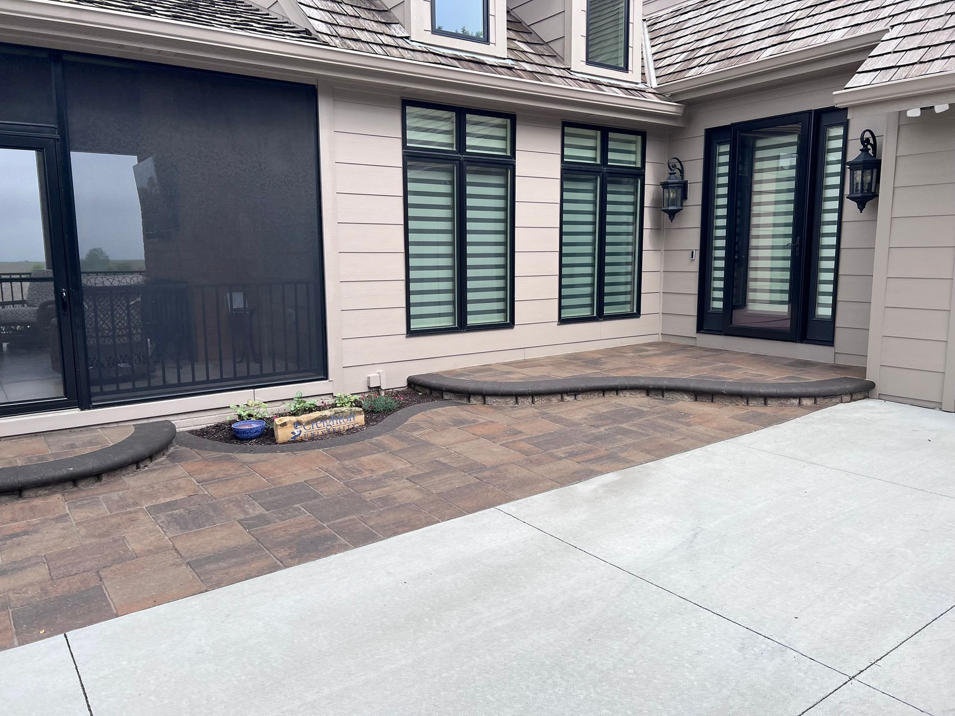 Exterior of a house with a brick patio, concrete driveway, and black-framed windows.