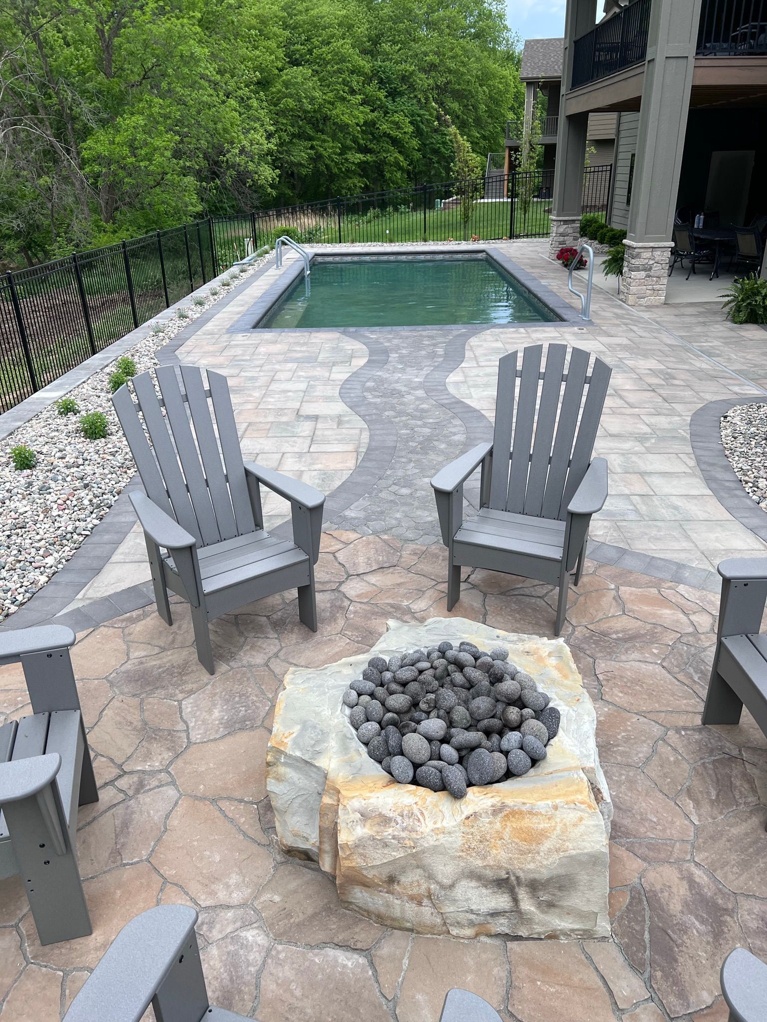 Patio with gray chairs around a stone fire pit, with a pool in the background.
