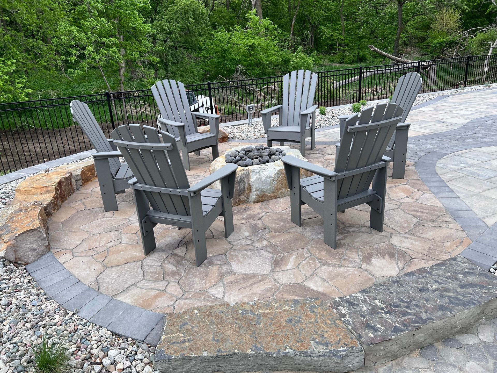 Six gray Adirondack chairs circle a fire pit on a stone patio.