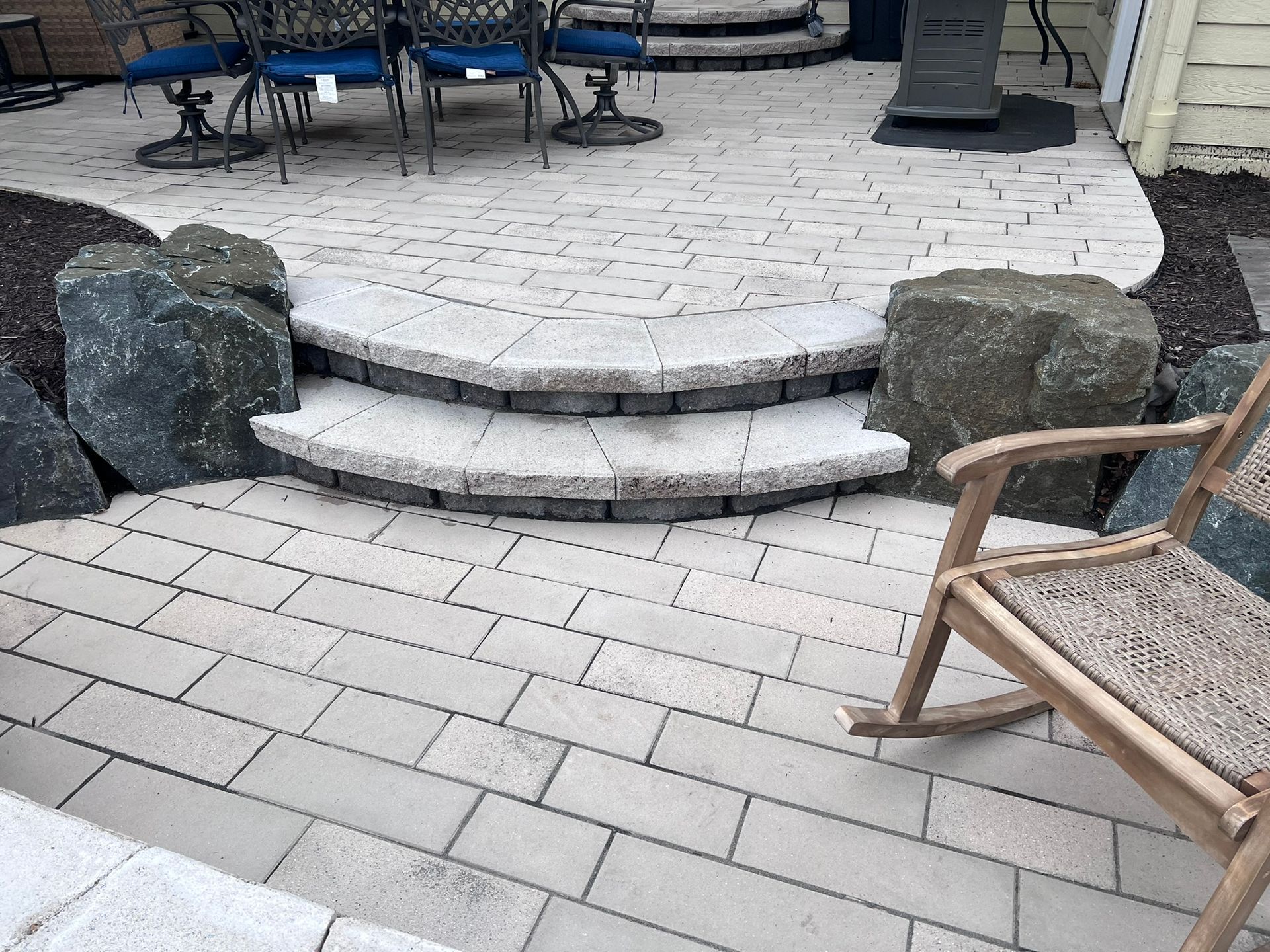 Paver patio with steps flanked by large rocks; a rocking chair sits nearby.