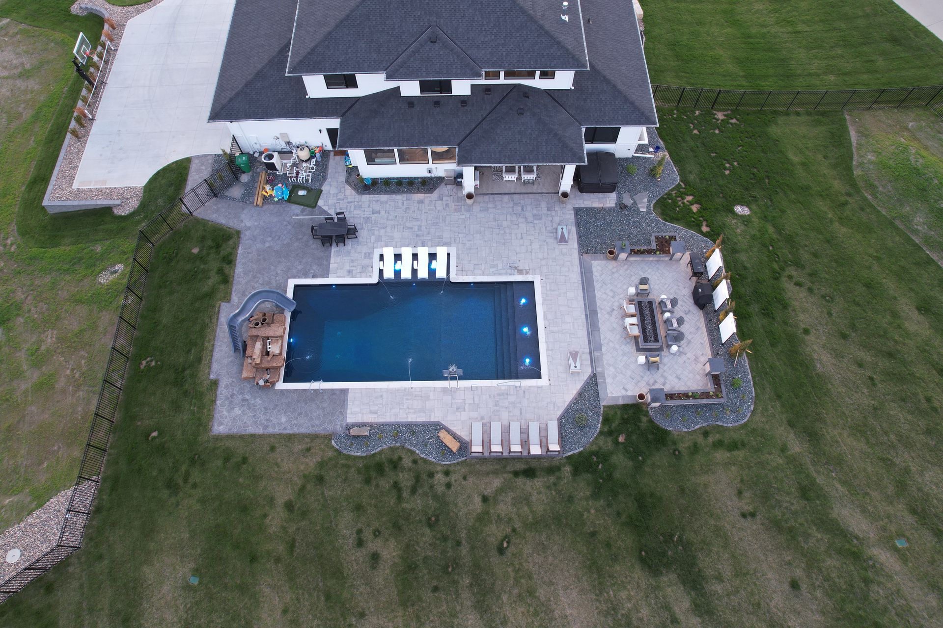 Aerial view of a modern house with a pool, patio, and landscaping on a grassy hill.