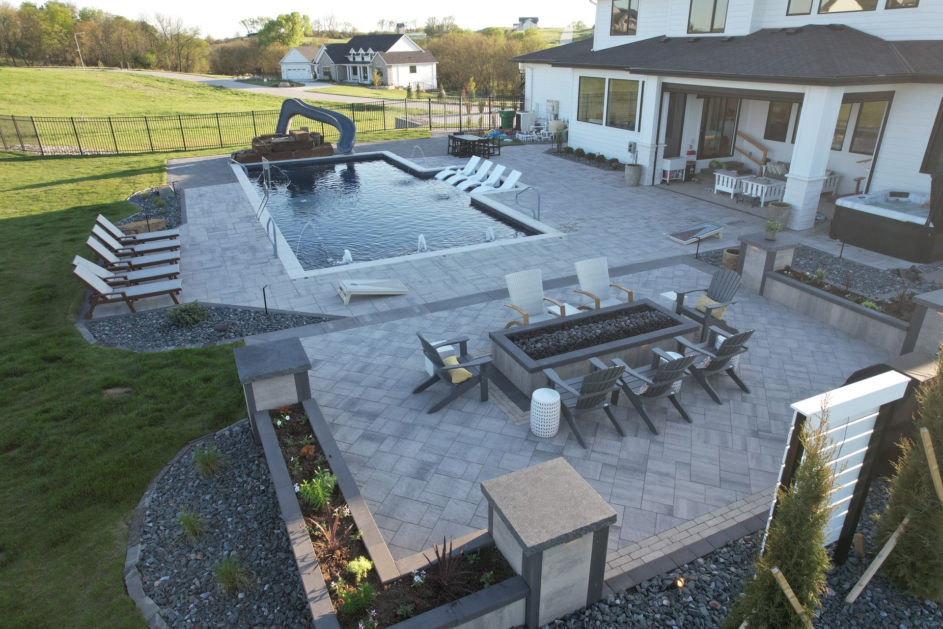Backyard patio with pool, fire pit, and seating; a modern white house is in the background.