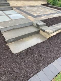 Stone steps lead to a paved patio area edged with dark mulch.